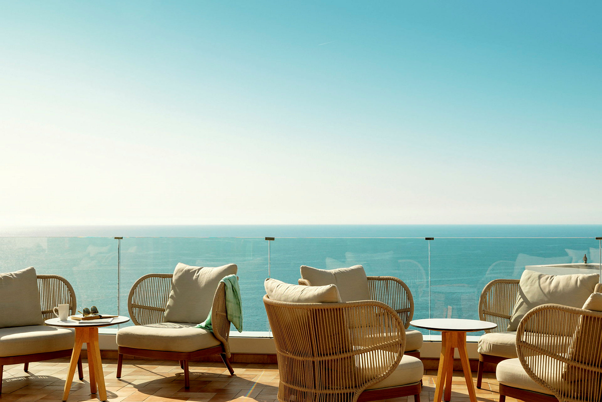 Loungeområde med sittmöbler, ett glasräcke och utsikt över havet. (AI-genererad text)