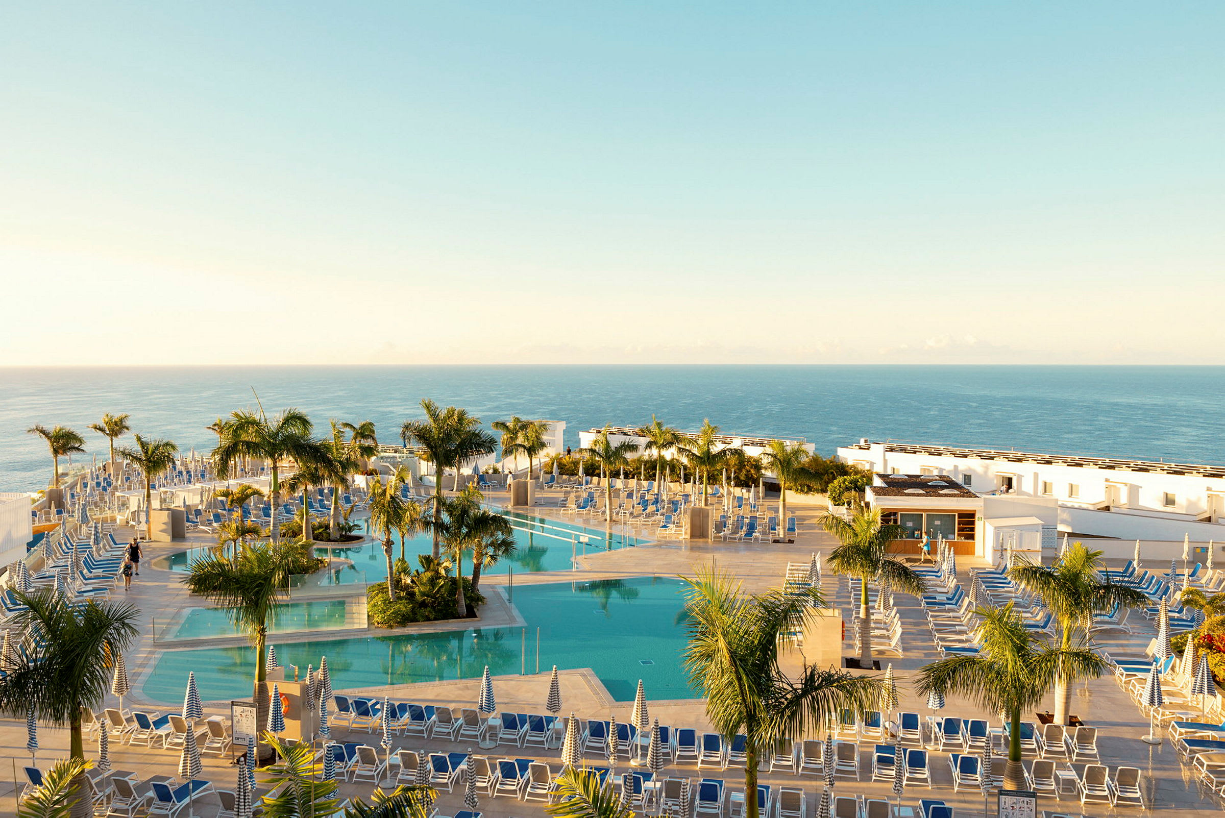 Hotellpoolområde med solstolar, parasoller och palmer vid havet. (AI-genererad text)