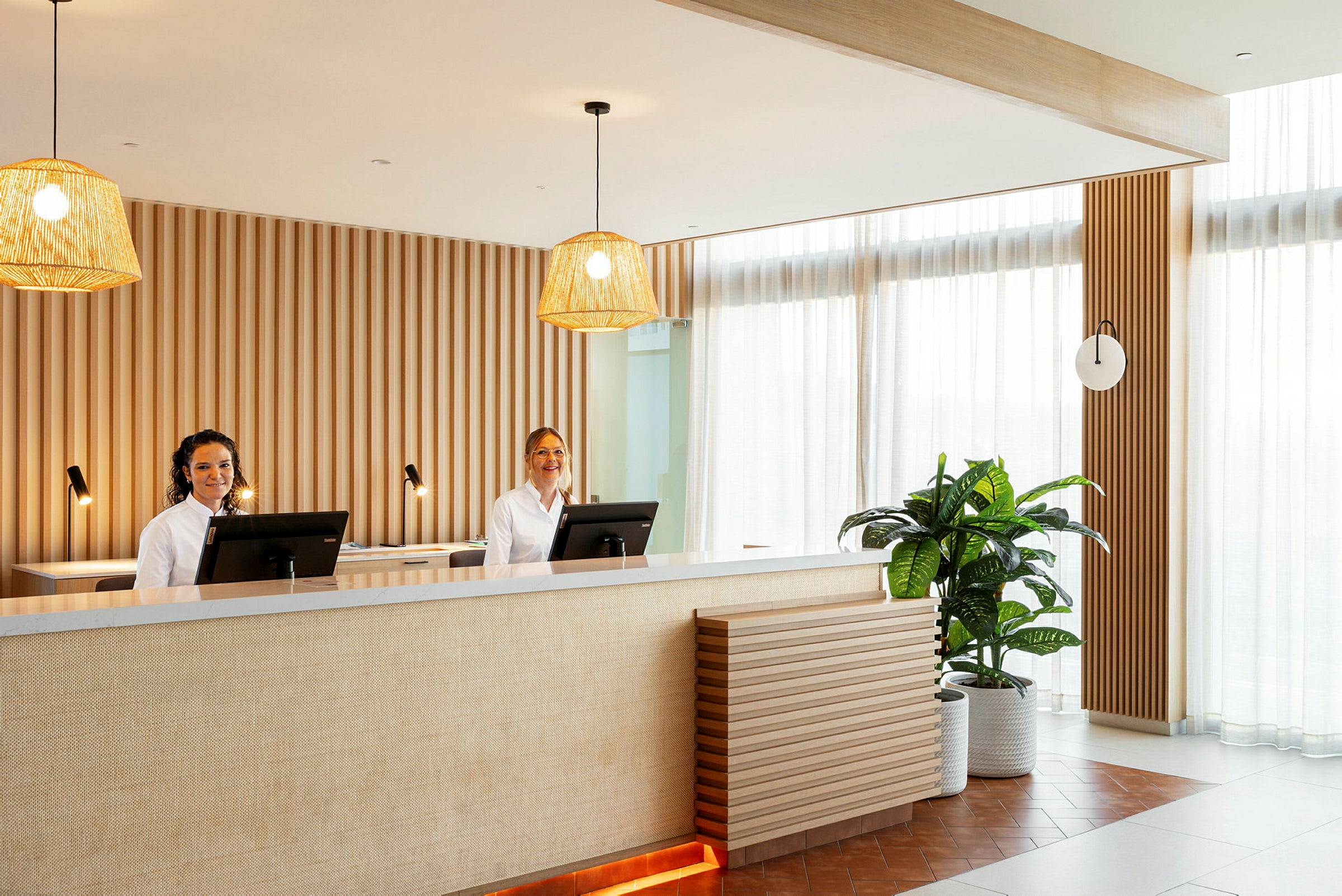 Reception med två arbetsstationer, hängande lampor och dekorativ växt. (AI-genererad text)