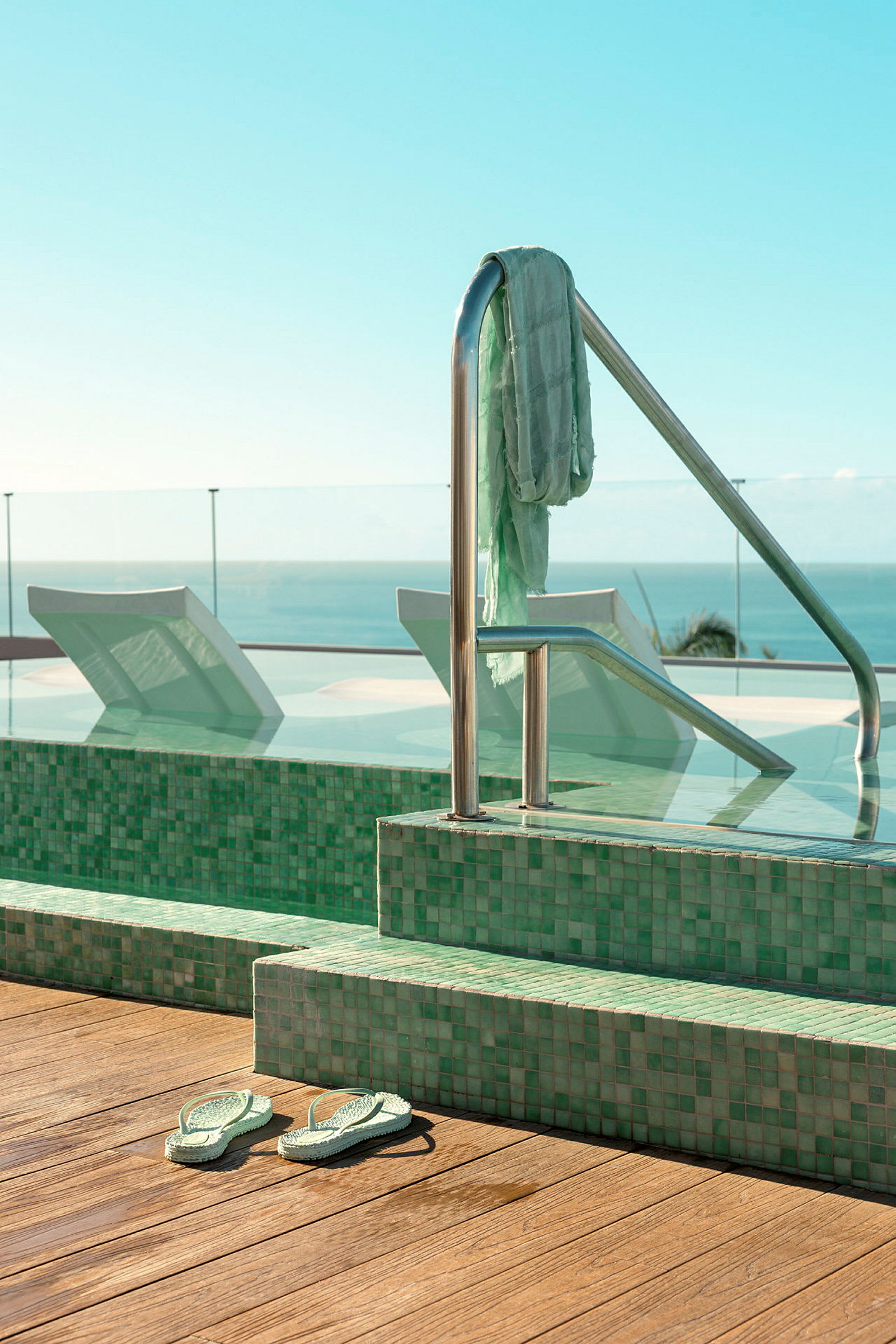 Bild på en pool med gröna kakelplattor och ett par sandaler intill. (AI-genererad text)