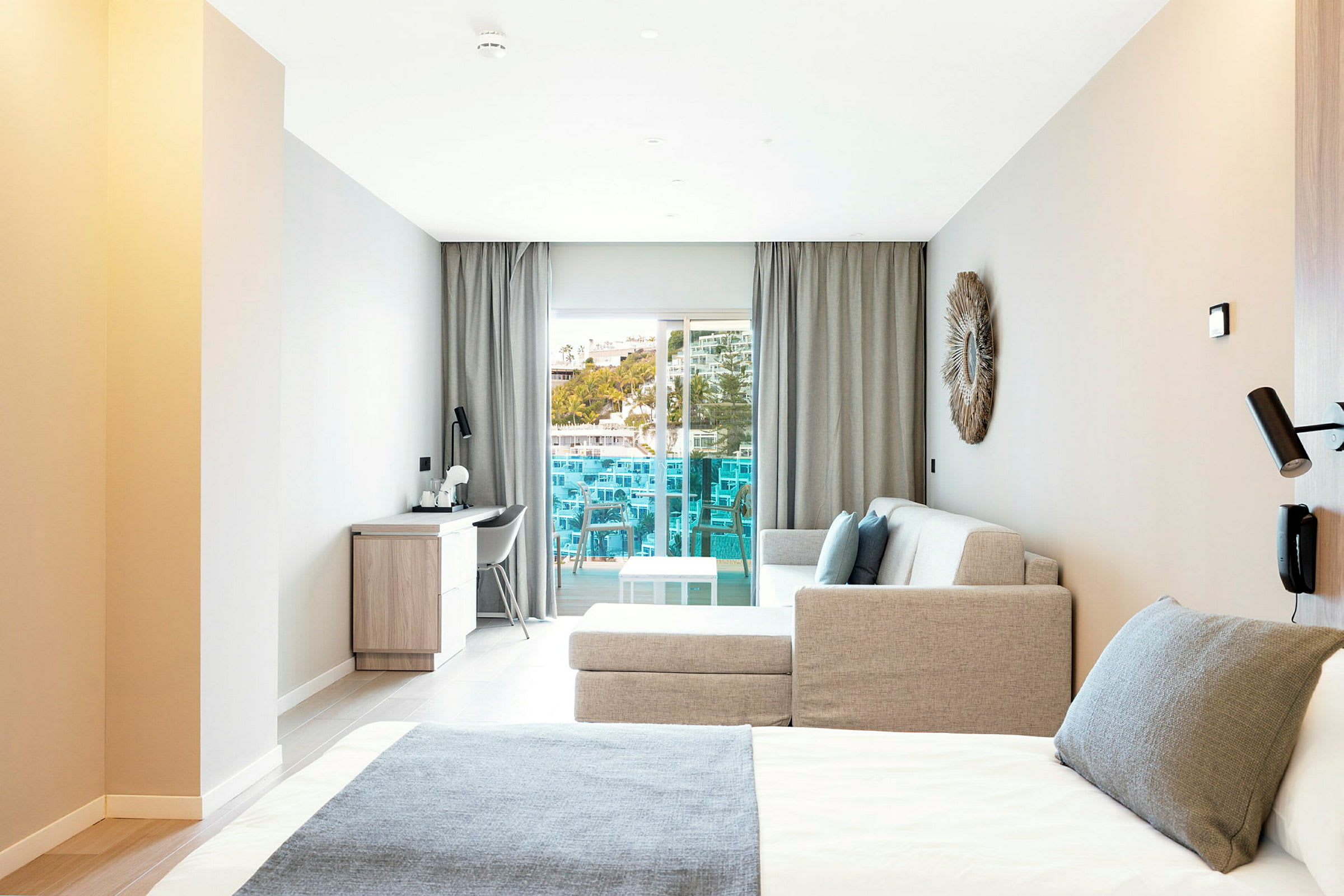 Modernt hotellrum med säng, soffa och skrivbord, samt en balkong med utsikt. (AI-genererad text)