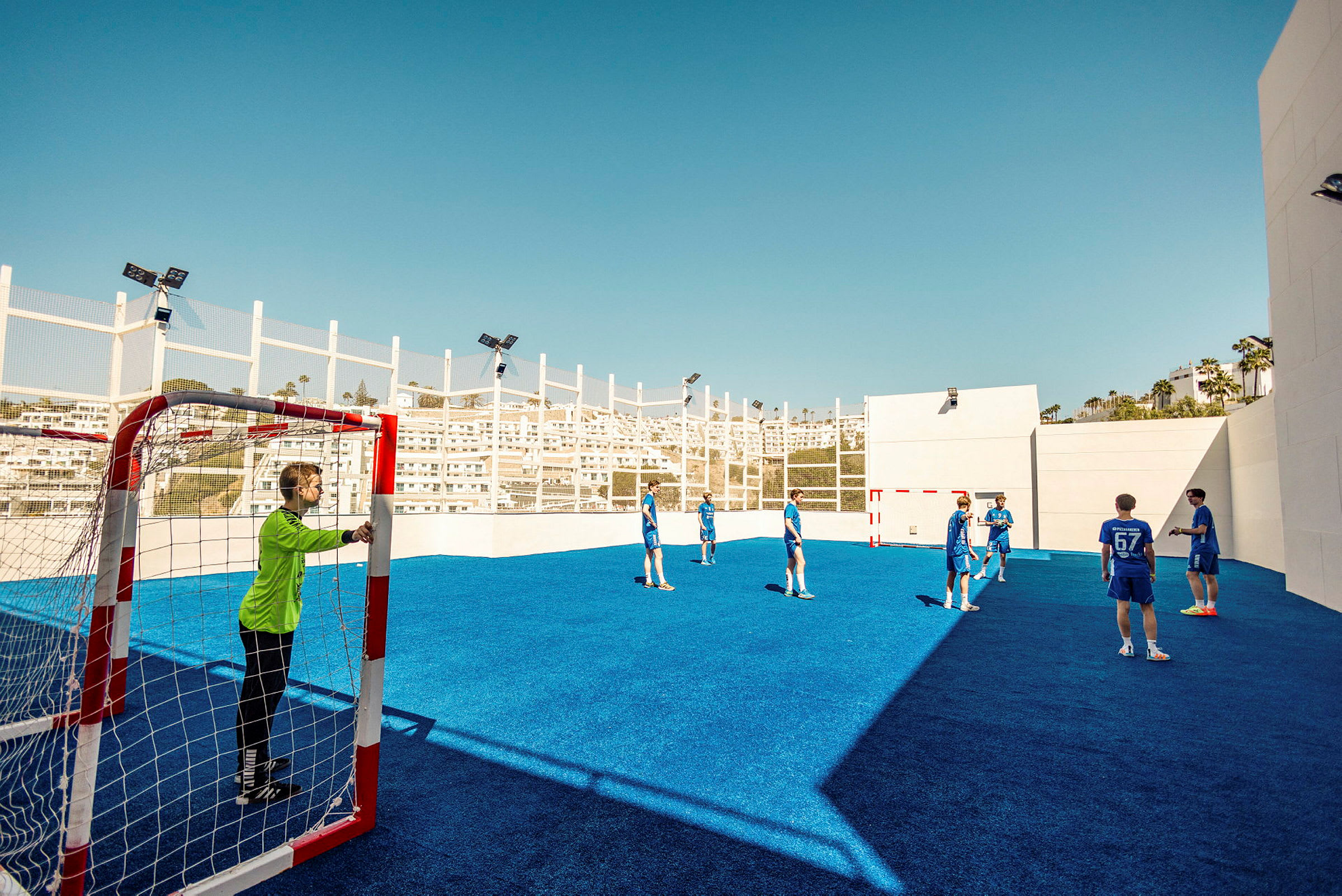 Flera personer spelar fotboll på en utomhusplan med blått underlag. (AI-genererad text)