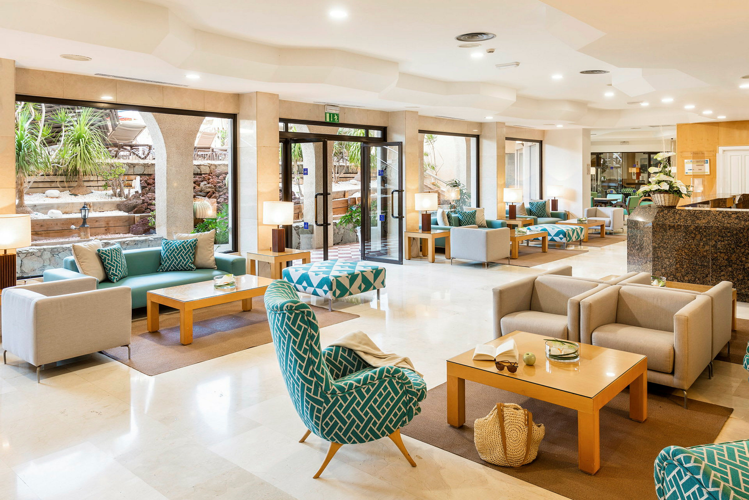 Hotellets lobby med sittplatser och soffgrupper samt stora fönster mot en utomhusgård. (AI-genererad text)