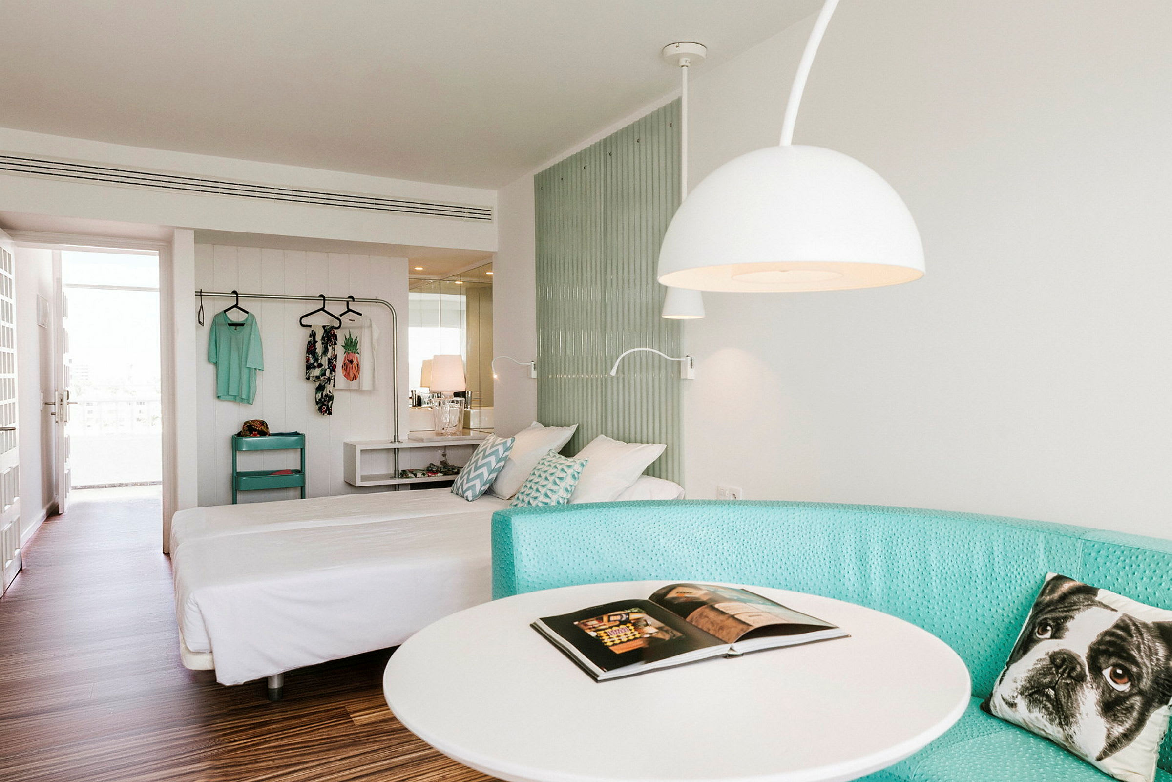 Ett hotellrum med en dubbelsäng, turkos soffa, ett runt bord och en hängande klädhållare. (AI-genererad text)