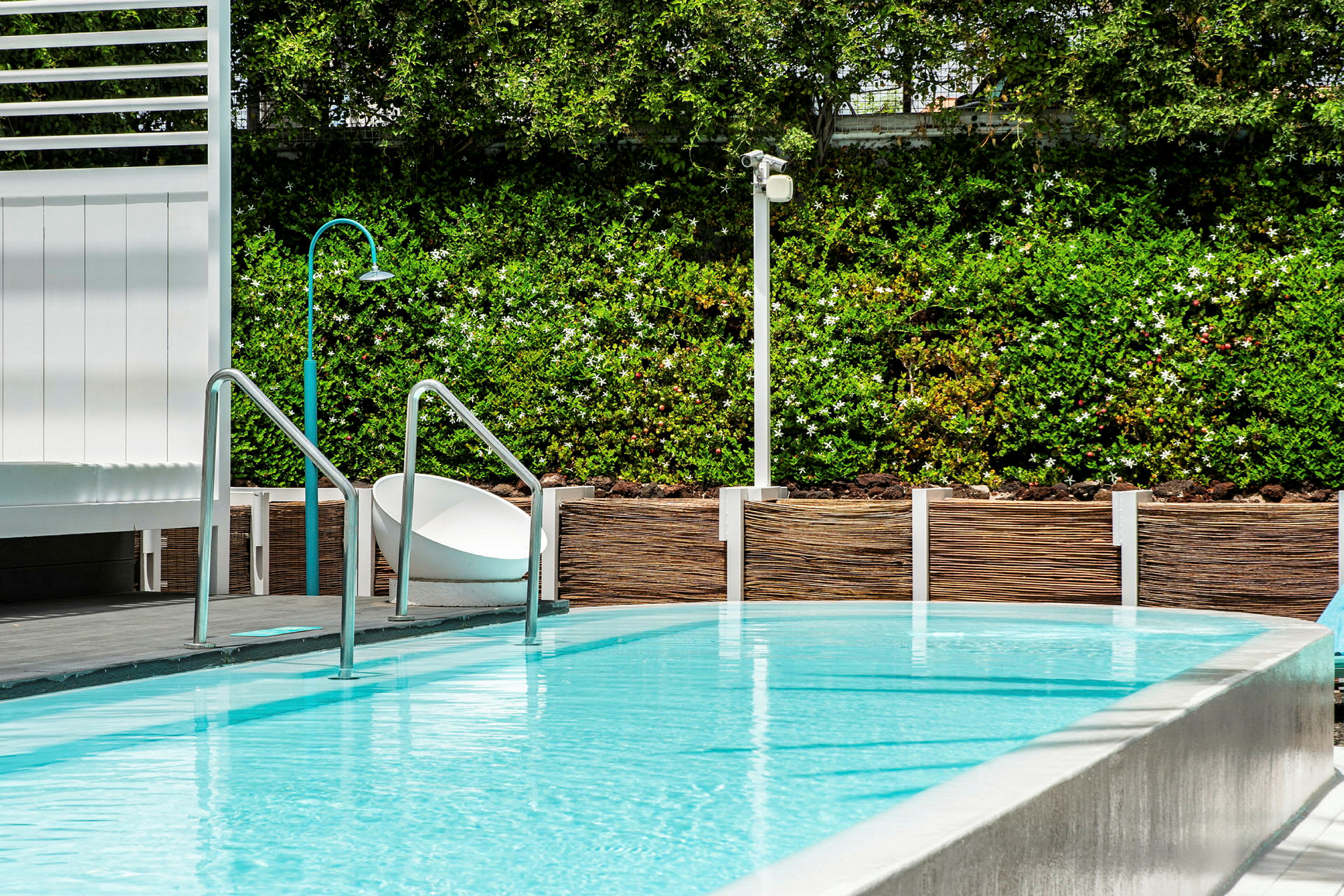En pool med metallsteg och grön växtlighet i bakgrunden. (AI-genererad text)