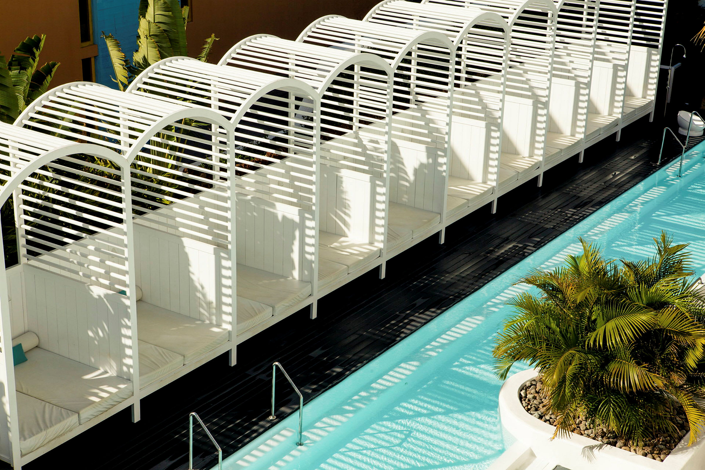 Vita baldakiner vid en blå swimmingpool, omgiven av grön växtlighet. (AI-genererad text)