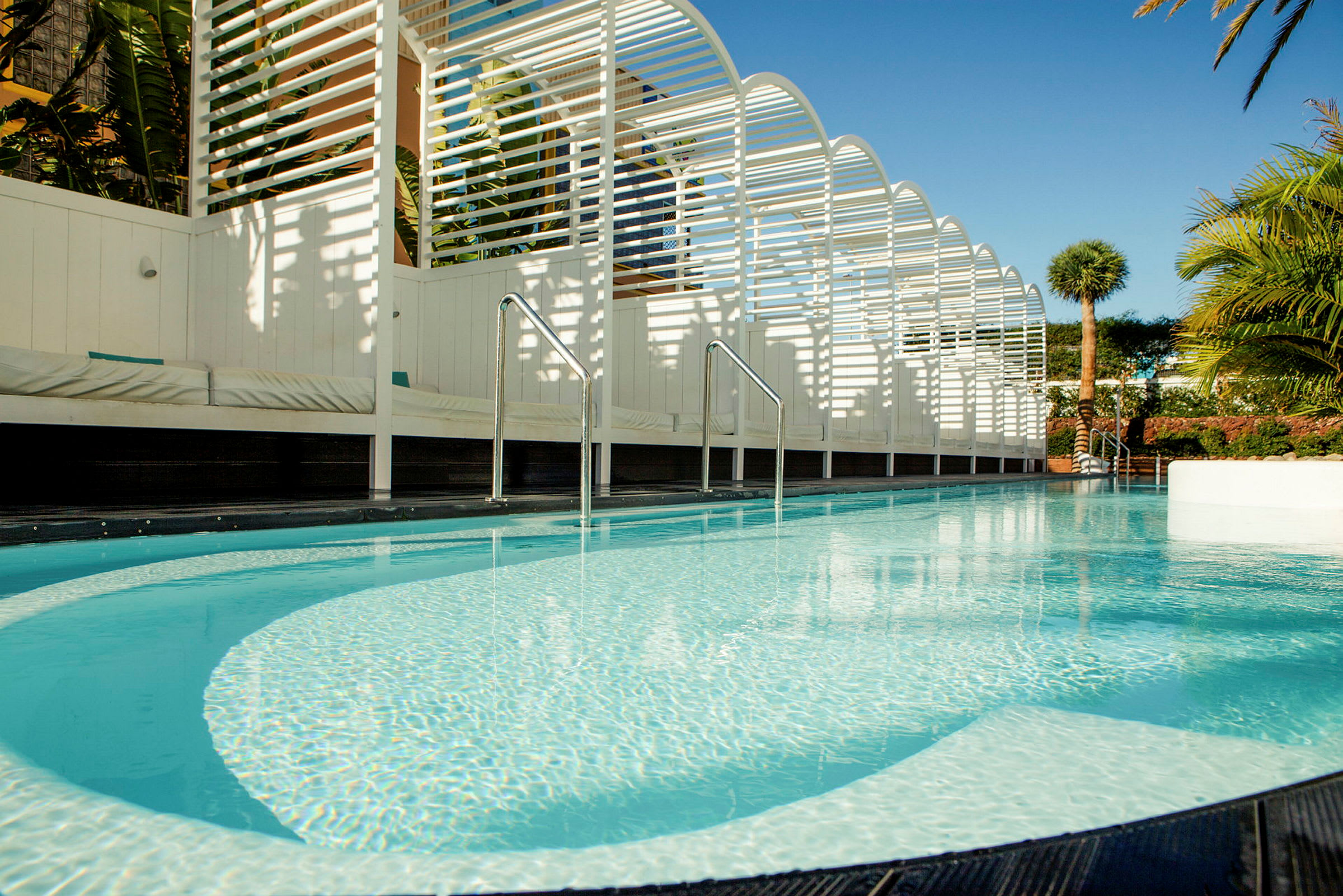 Pool med klart vatten och omgivande vit struktur samt grönska. (AI-genererad text)