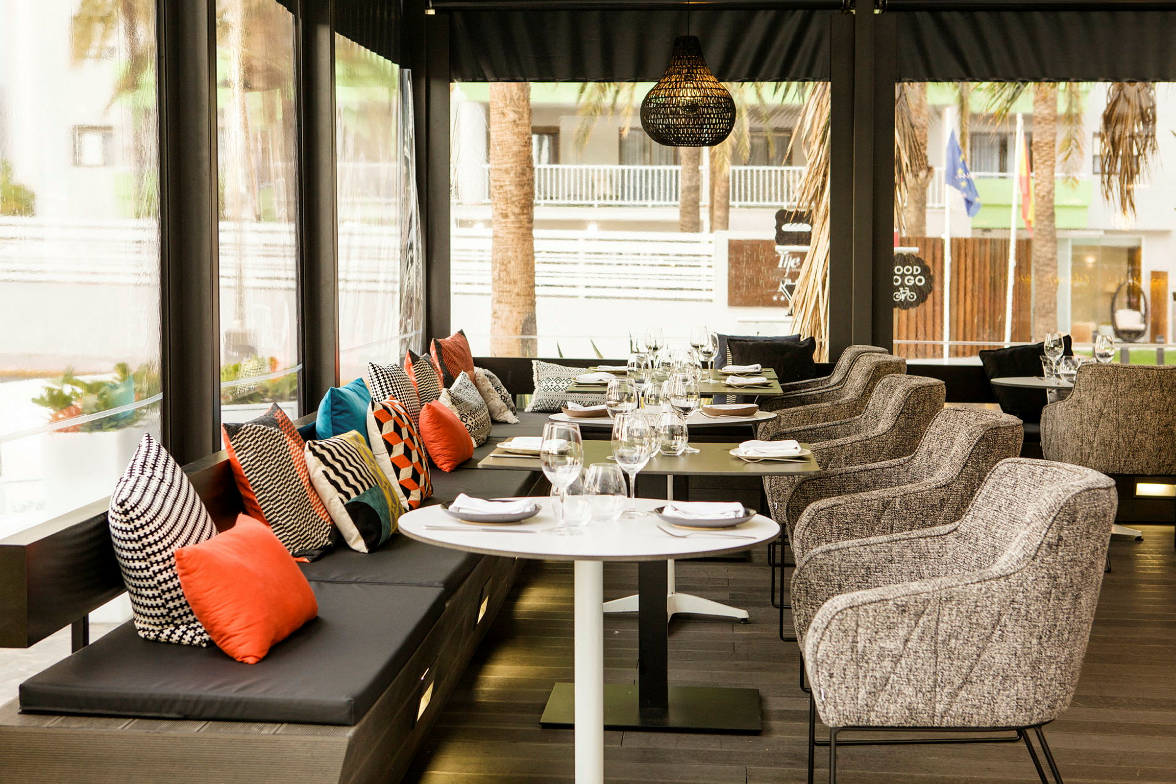 En restaurang med bord och stolar, samt en sittbänk med färgglada kuddar. (AI-genererad text)