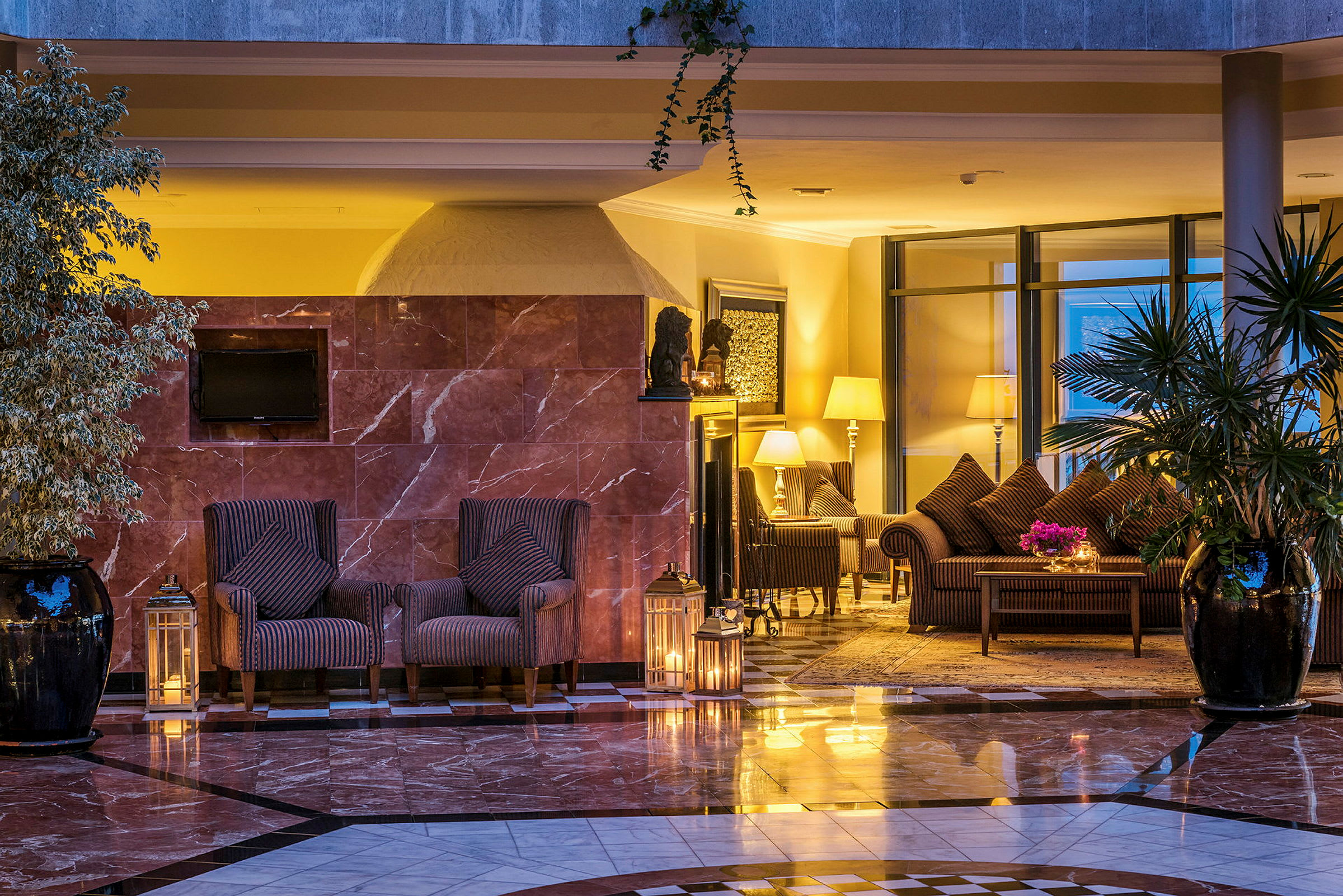 Ett hotellrum med elegant inredning, inklusive fåtöljer, bord, lampskärmar och växter. (AI-genererad text)