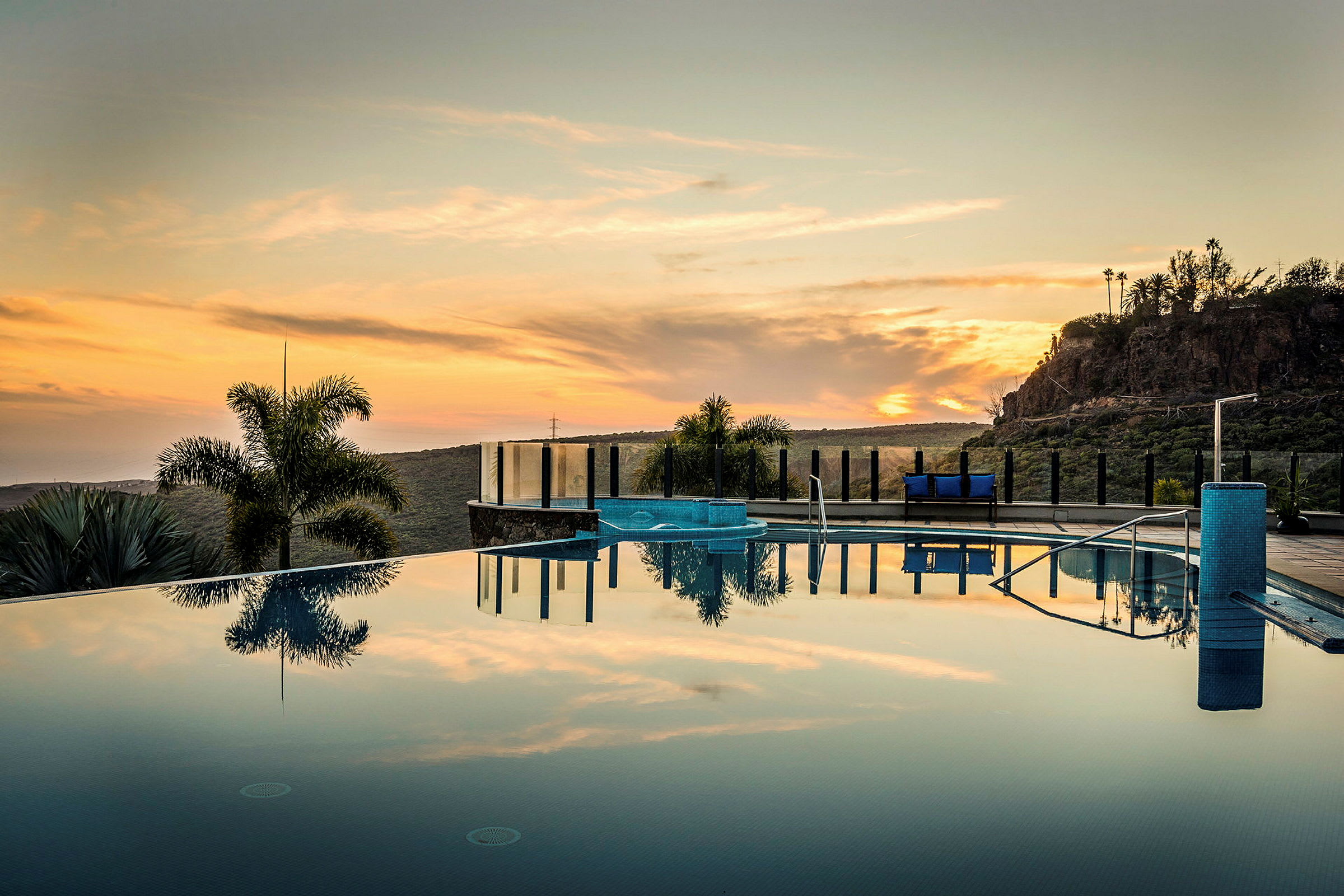 En infinitypool med utsikt mot en solnedgång över ett kuperat landskap. (AI-genererad text)