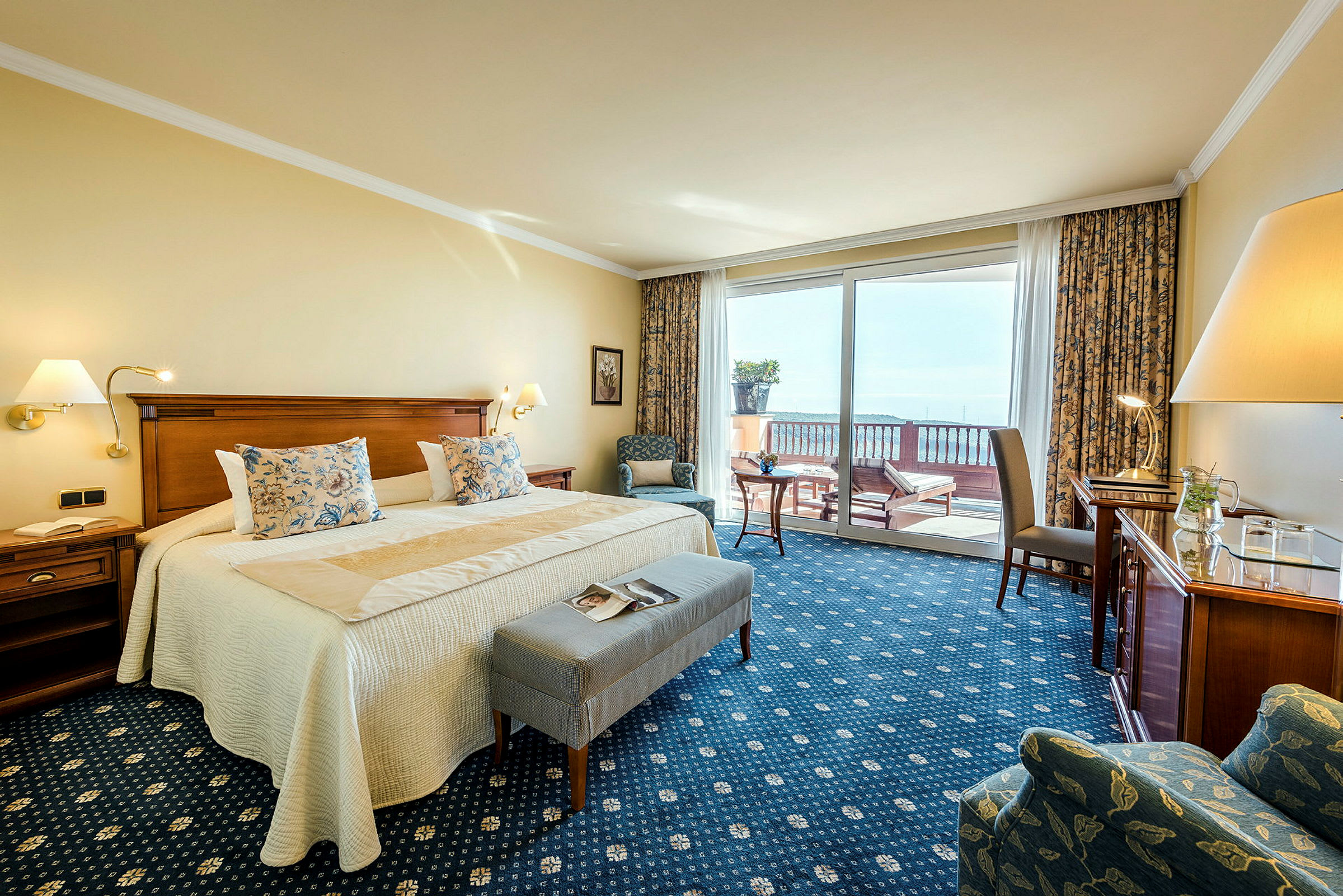 Hotellrum med dubbelsäng och sittgrupp, samt balkong med utsikt. (AI-genererad text)