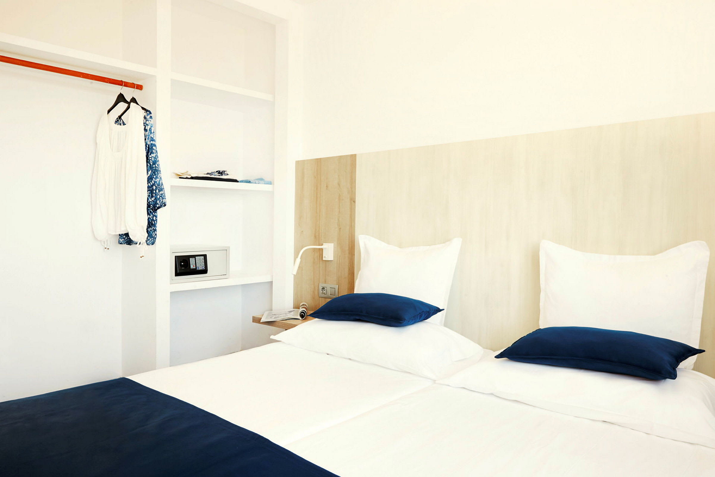 Ett hotellrum med två sängar med vita och blå sängkläder, en garderob med kläder och ett kassaskåp. (AI-genererad text)