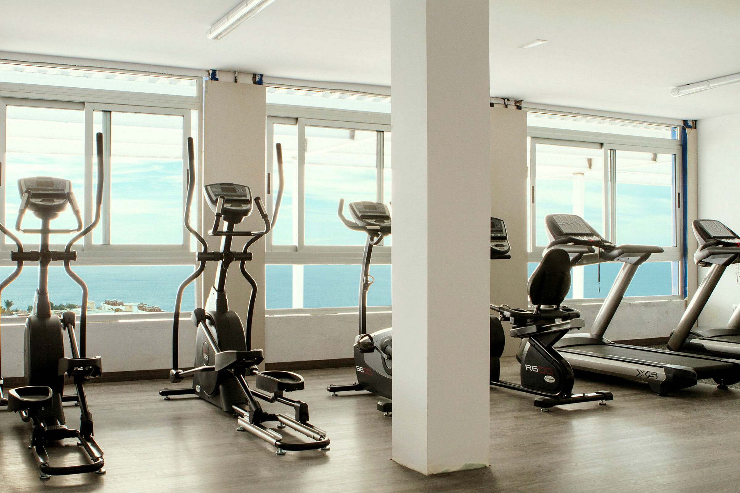 Gym med träningsmaskiner framför fönster med havsutsikt. (AI-genererad text)