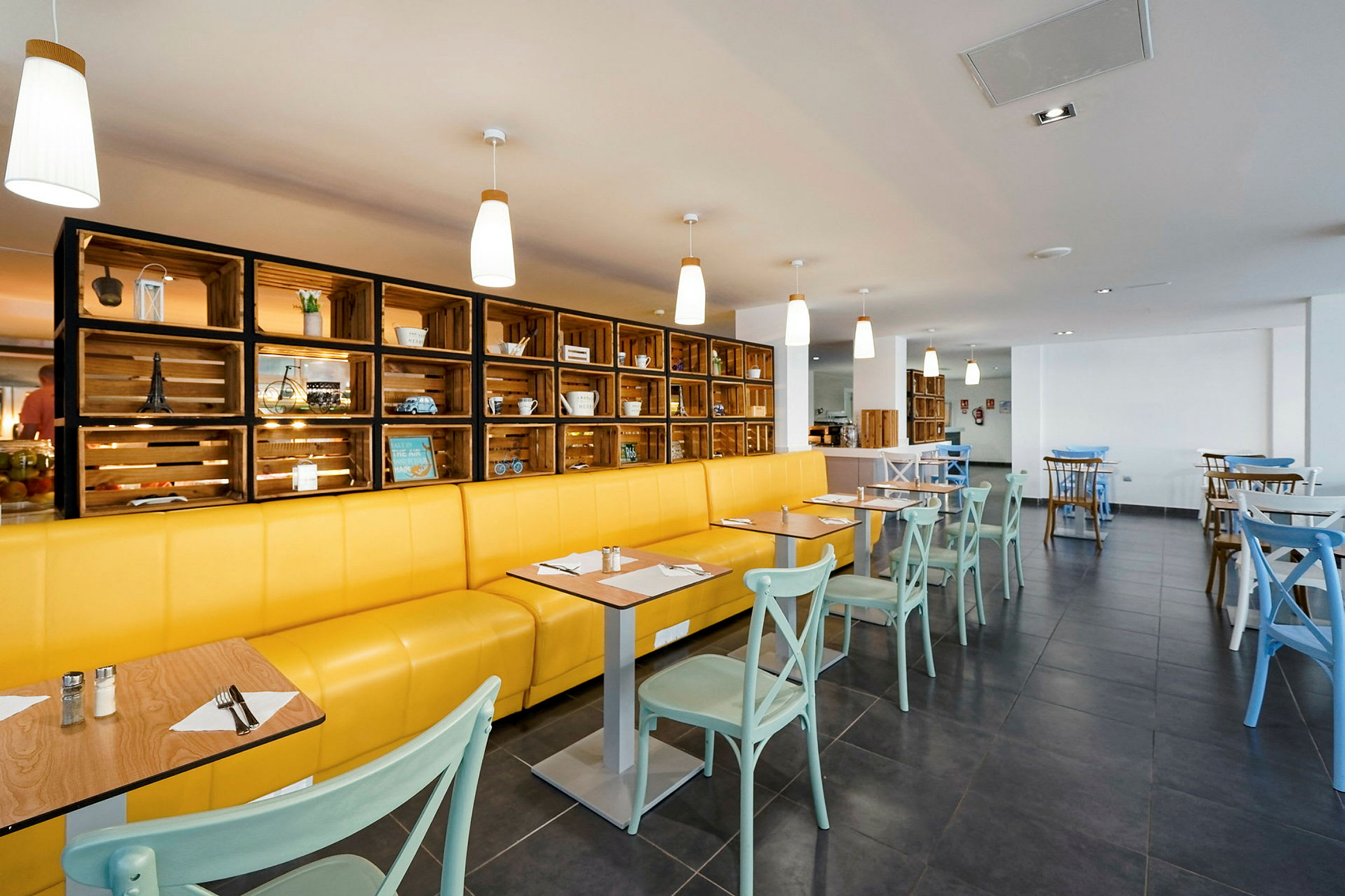 Restaurang med gul soffa, ljusa stolar och dekorativ trähylla. (AI-genererad text)