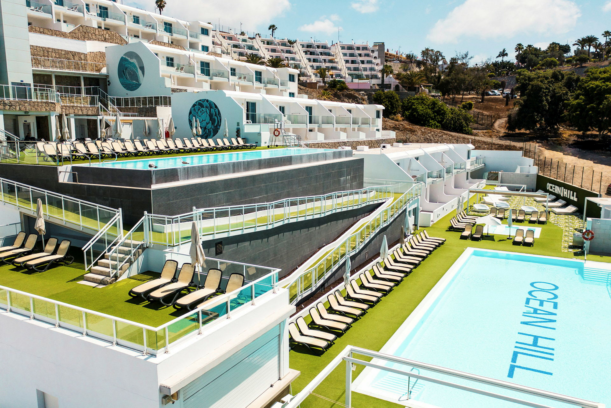 Bild av en resort med poolområden, solstolar och flera våningsplan mot en sluttning. (AI-genererad text)