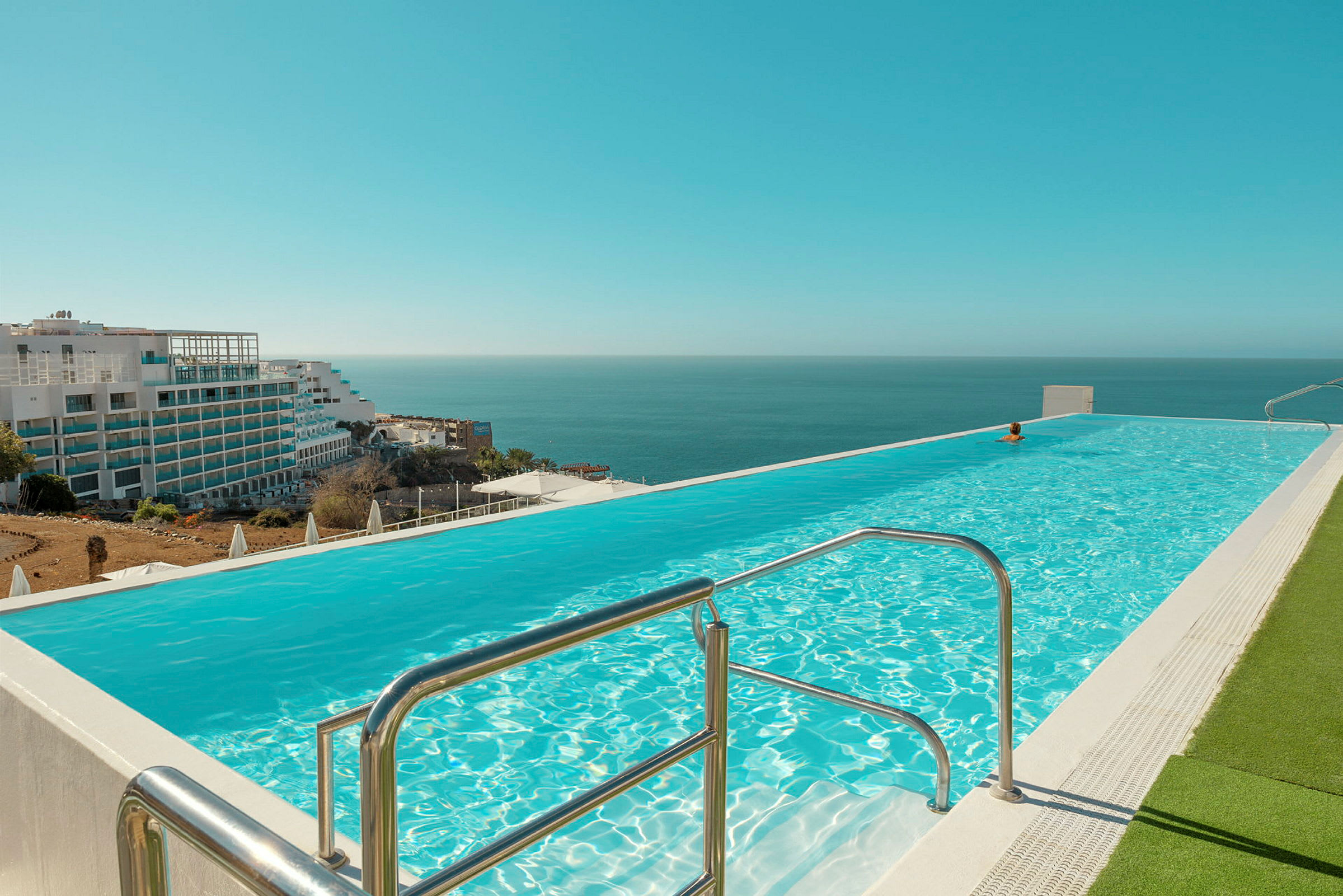 Infinitypool med utsikt mot havet. Byggnader synliga i bakgrunden. (AI-genererad text)
