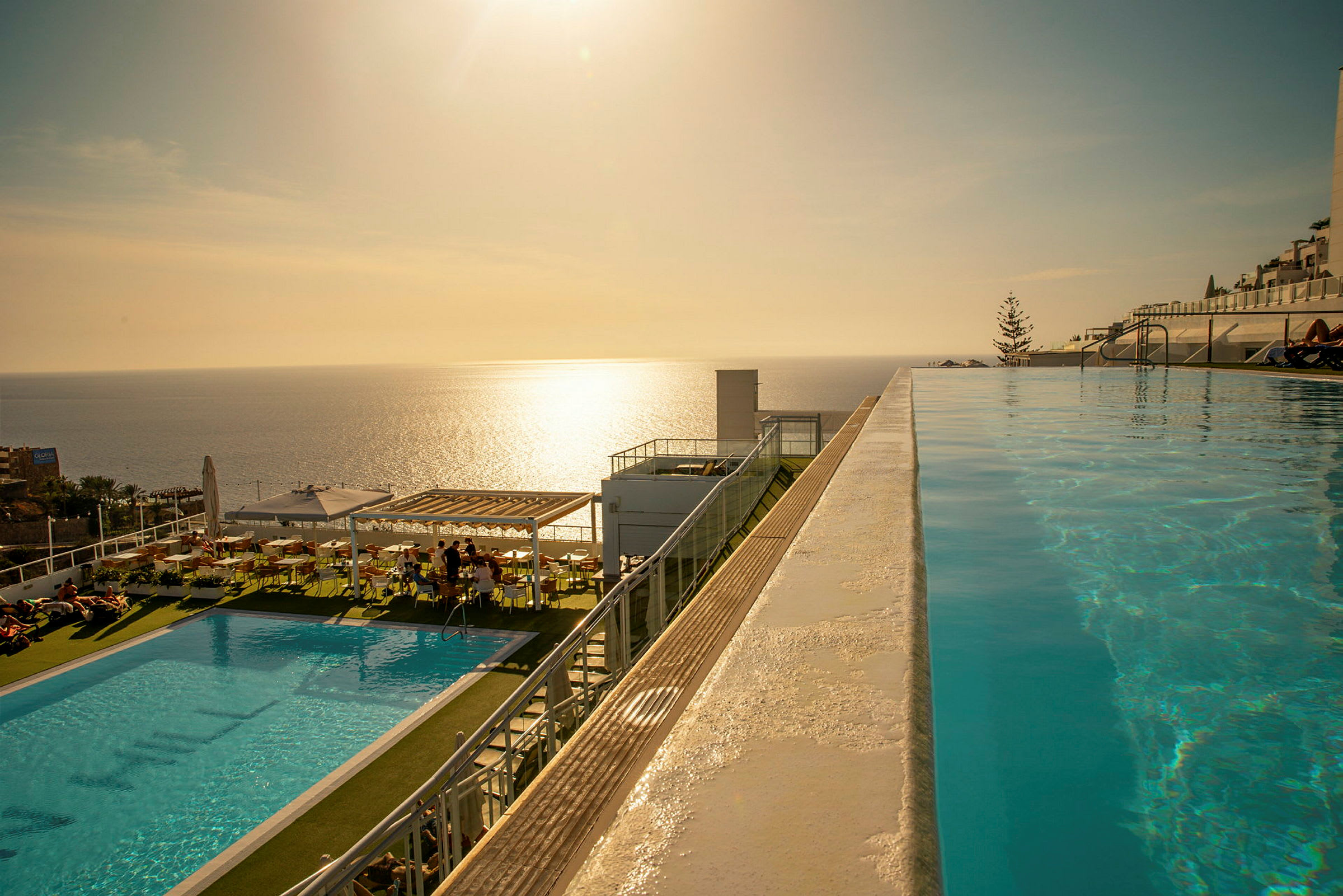 Infinitypool med utsikt över havet vid solnedgången, med sittplatser och en mindre pool intill. (AI-genererad text)