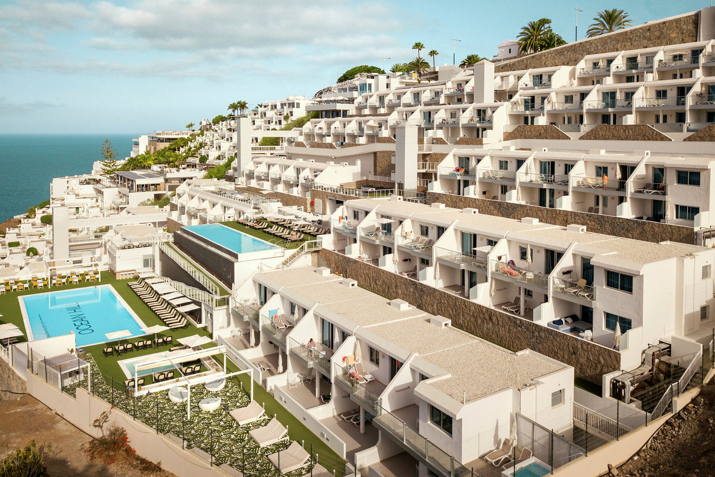 Hotellbyggnad med flera våningar och pool mot havet. (AI-genererad text)