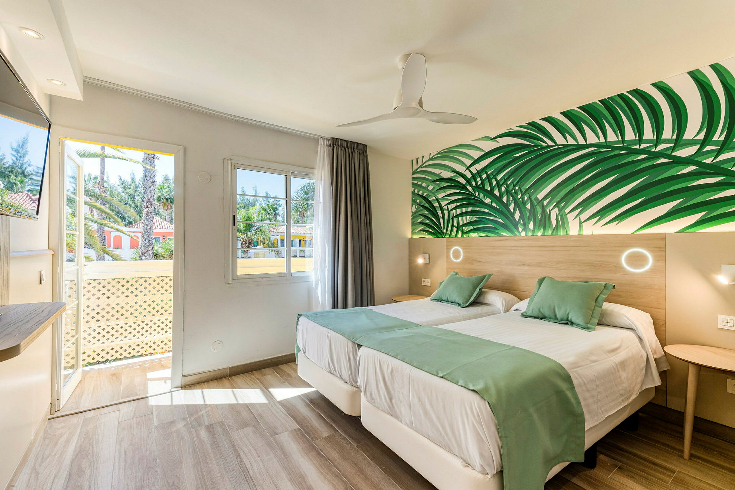 Interiör av ett hotellrum med två enkelsängar, gröna dekorativa detaljer och väggmålning av blad. (AI-genererad text)