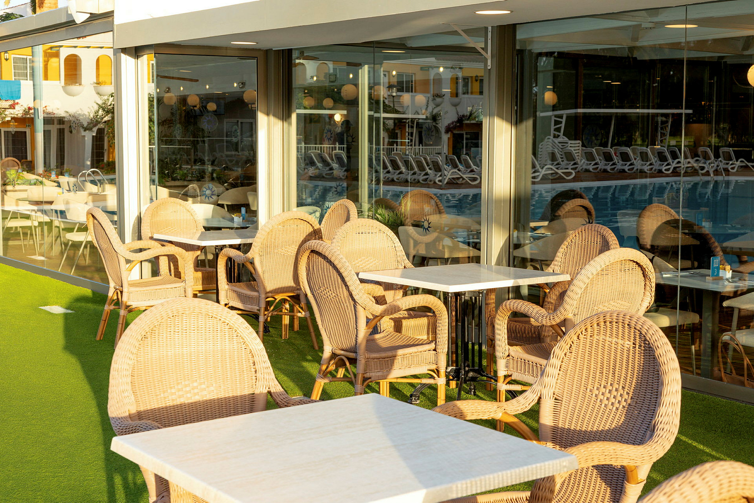 Utemöbler vid ett café eller restaurang, med flätade stolar och bord, placerade bredvid stora fönster. (AI-genererad text)