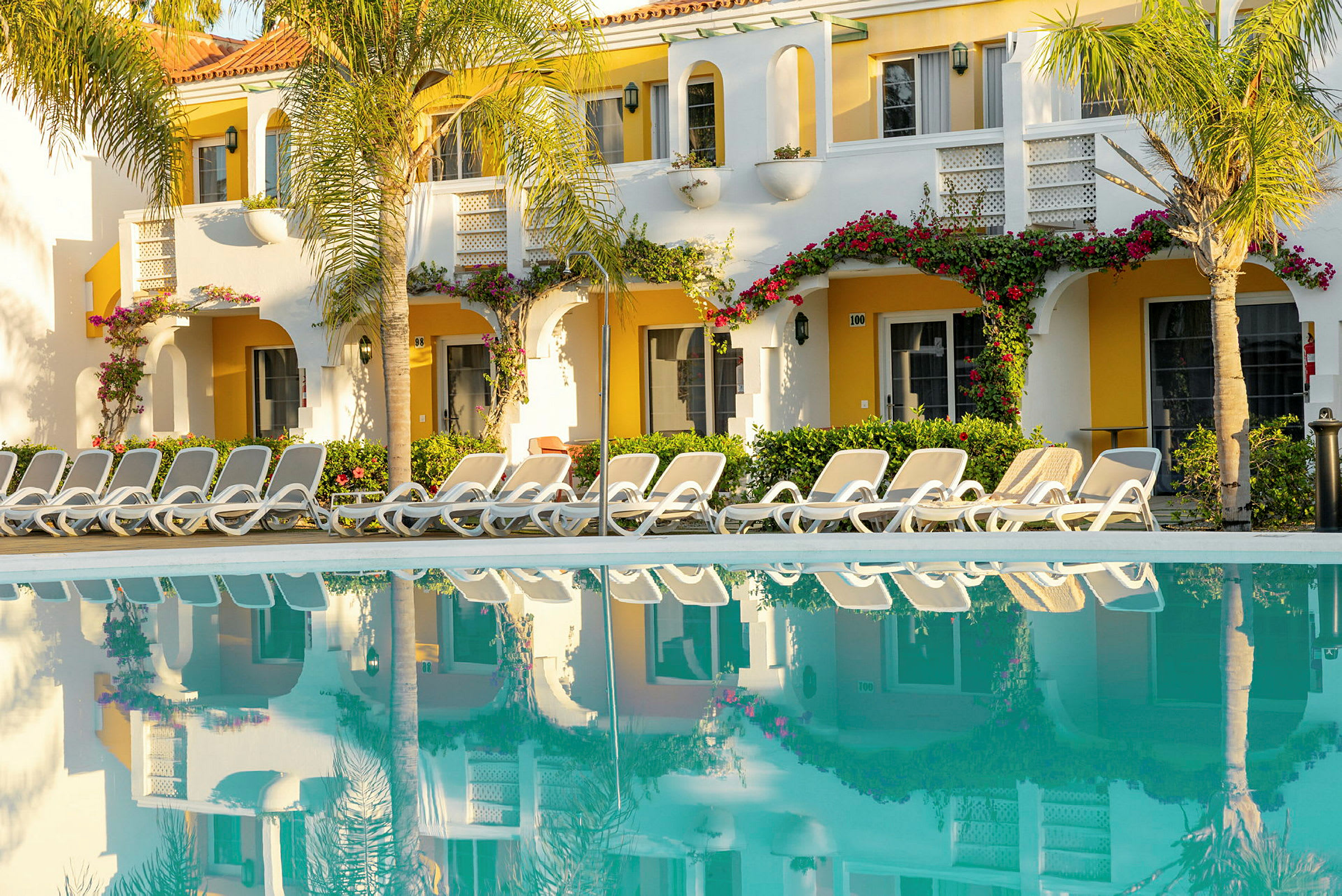 En pool framför ett hotell med solstolar och grönska. (AI-genererad text)