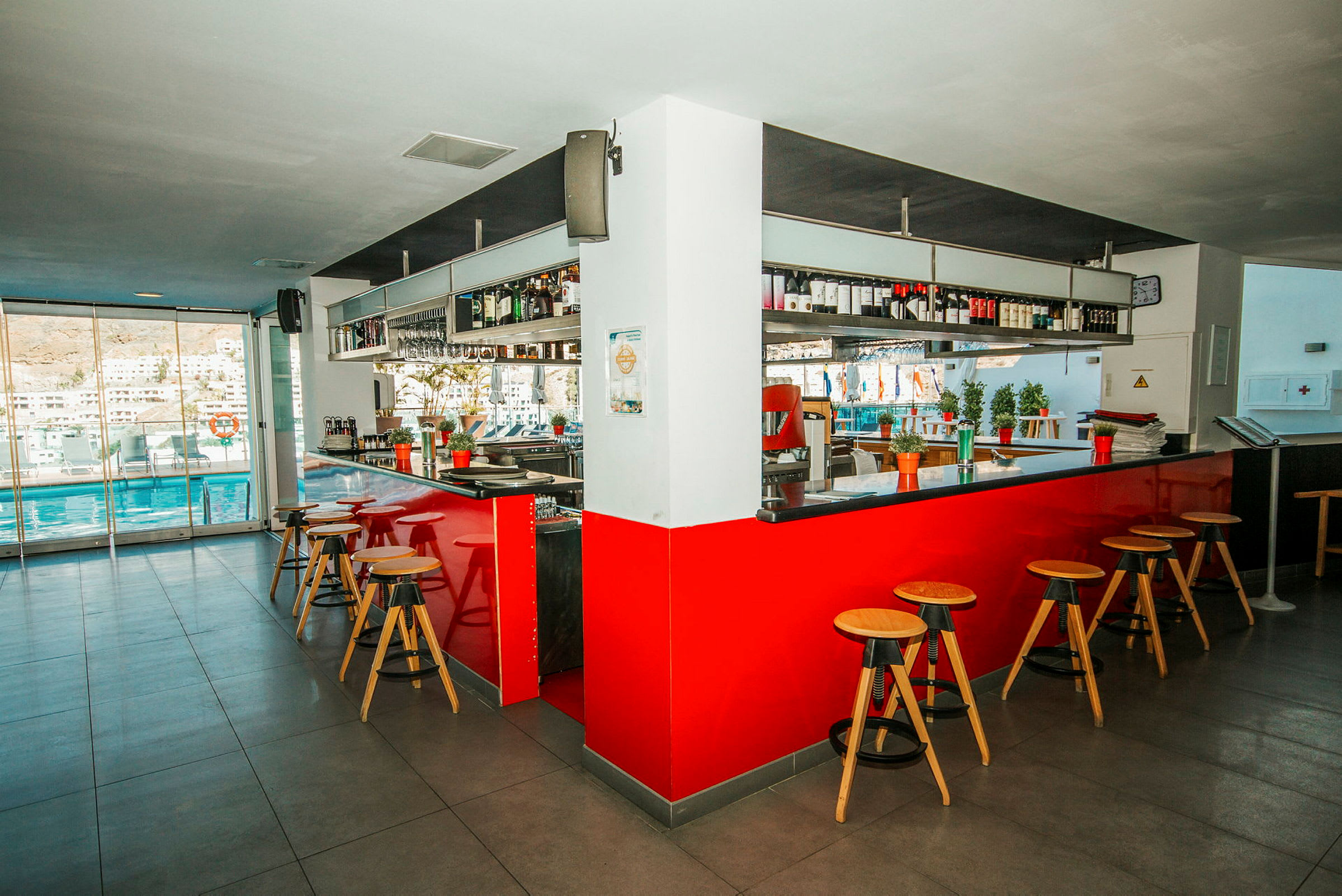 Inomhusbild av en bar med röda detaljer och höga träpallar intill en bardisk. (AI-genererad text)