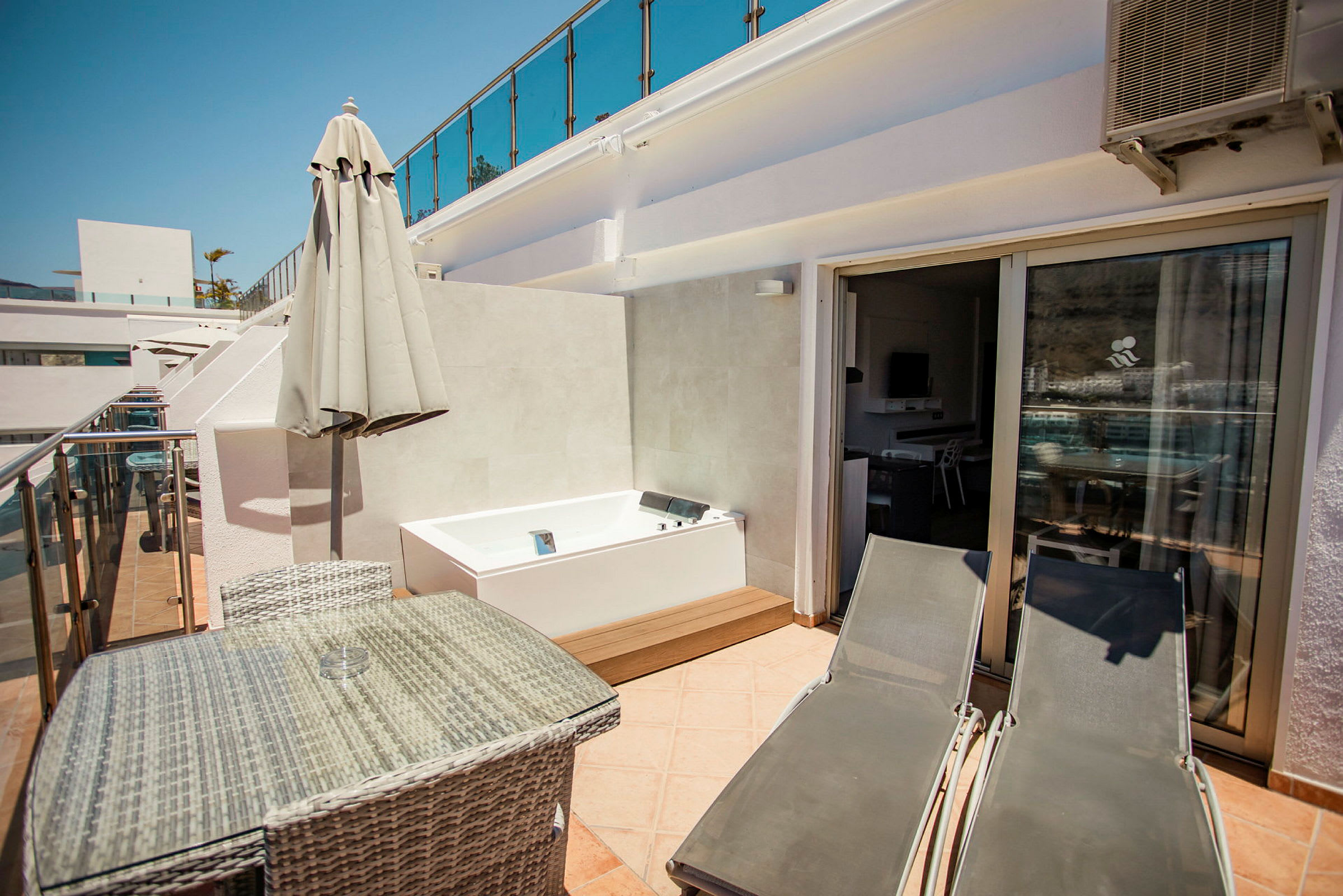 Privat terrass med bord, stolar, solstolar och ett bubbelbad. (AI-genererad text)