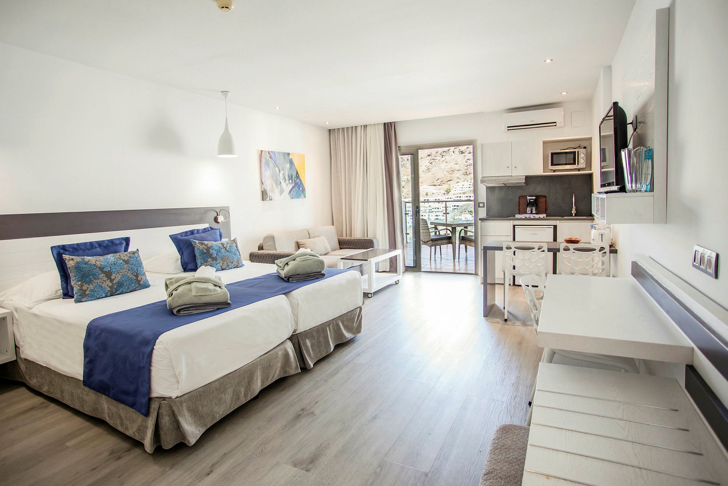 Modernt hotellrum med två sängar, sittgrupp, kök och balkong. (AI-genererad text)