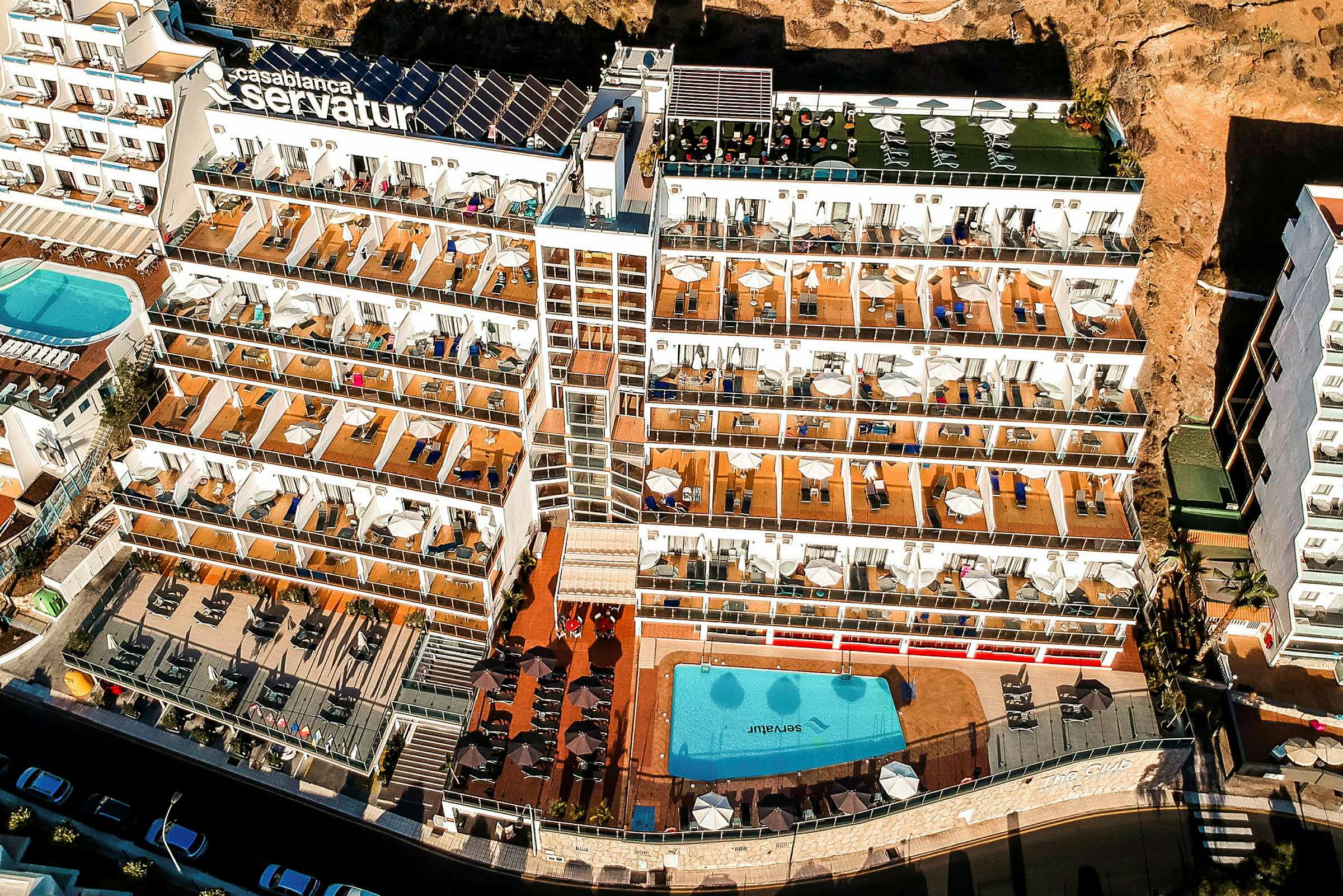 Flygfoto av ett hotellkomplex med flera våningar, stora balkonger och en poolområde. (AI-genererad text)