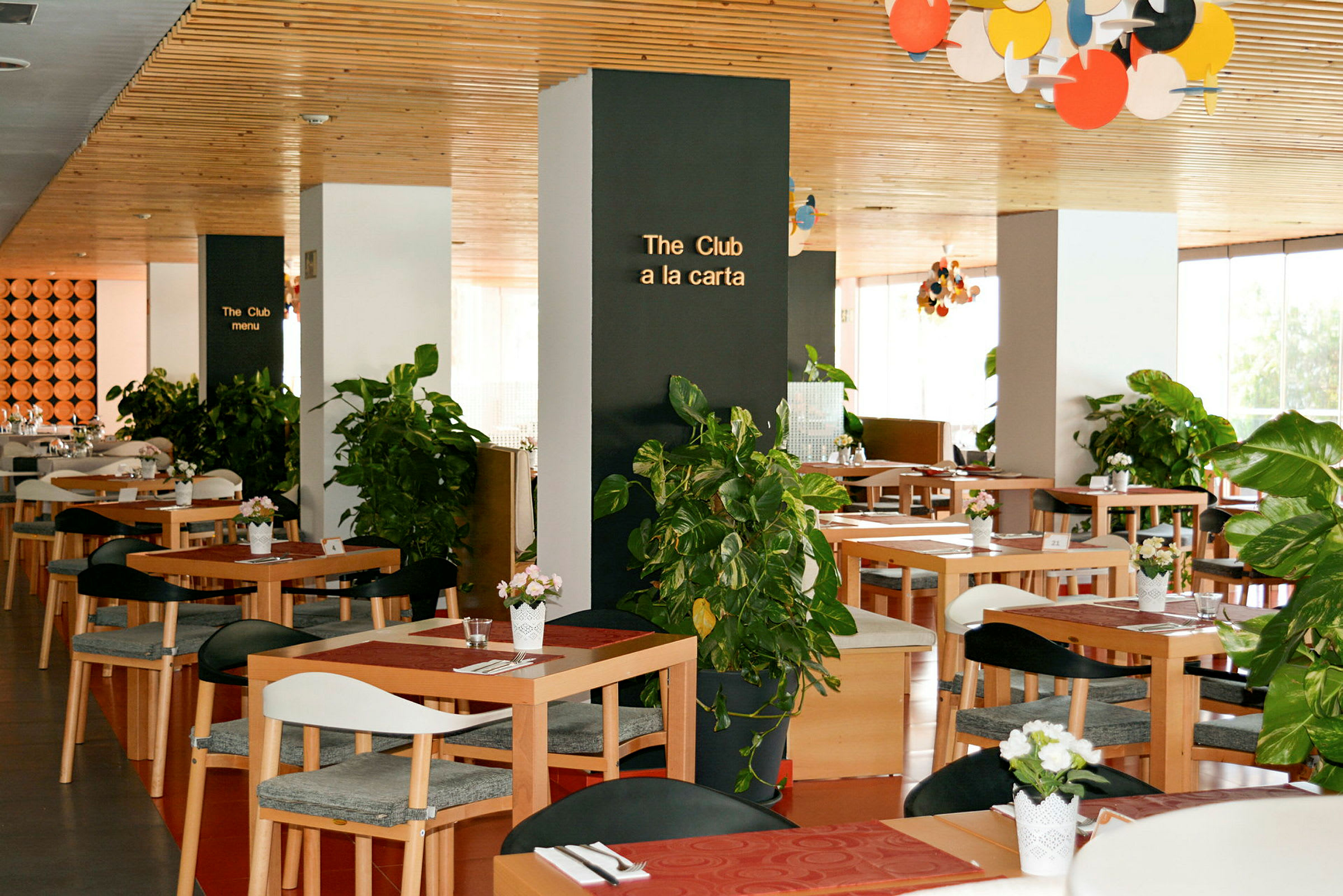 En restaurang med träbord och dekorationer av gröna växter. (AI-genererad text)