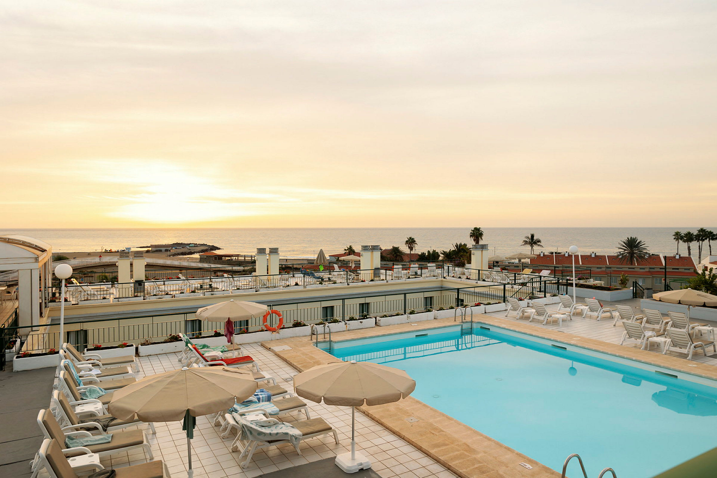 En hotellpool med solstolar och parasoller, med utsikt över havet under solnedgången. (AI-genererad text)