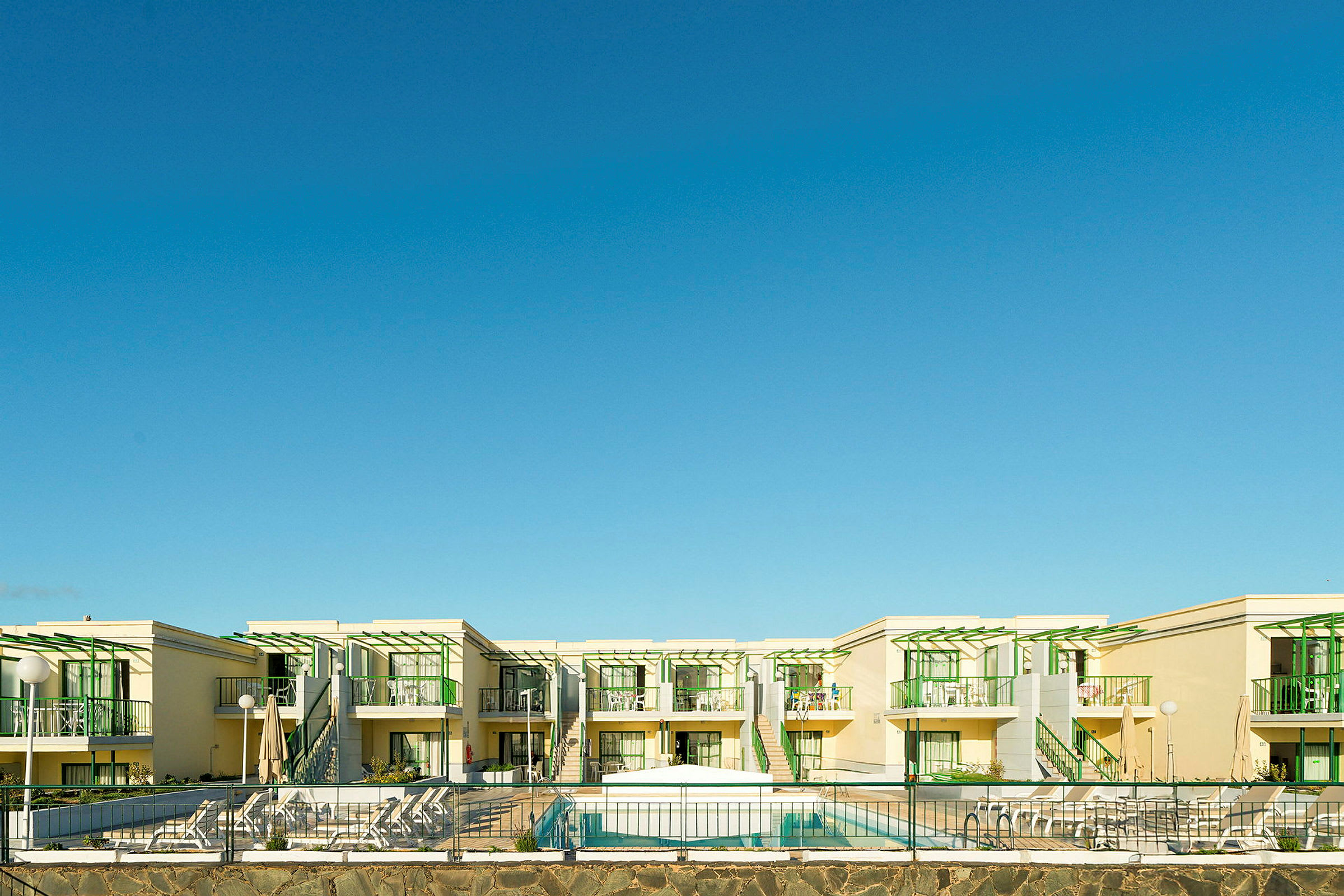 Ett hotellkomplex med moderna byggnader med gröna detaljer och en pool framför. (AI-genererad text)
