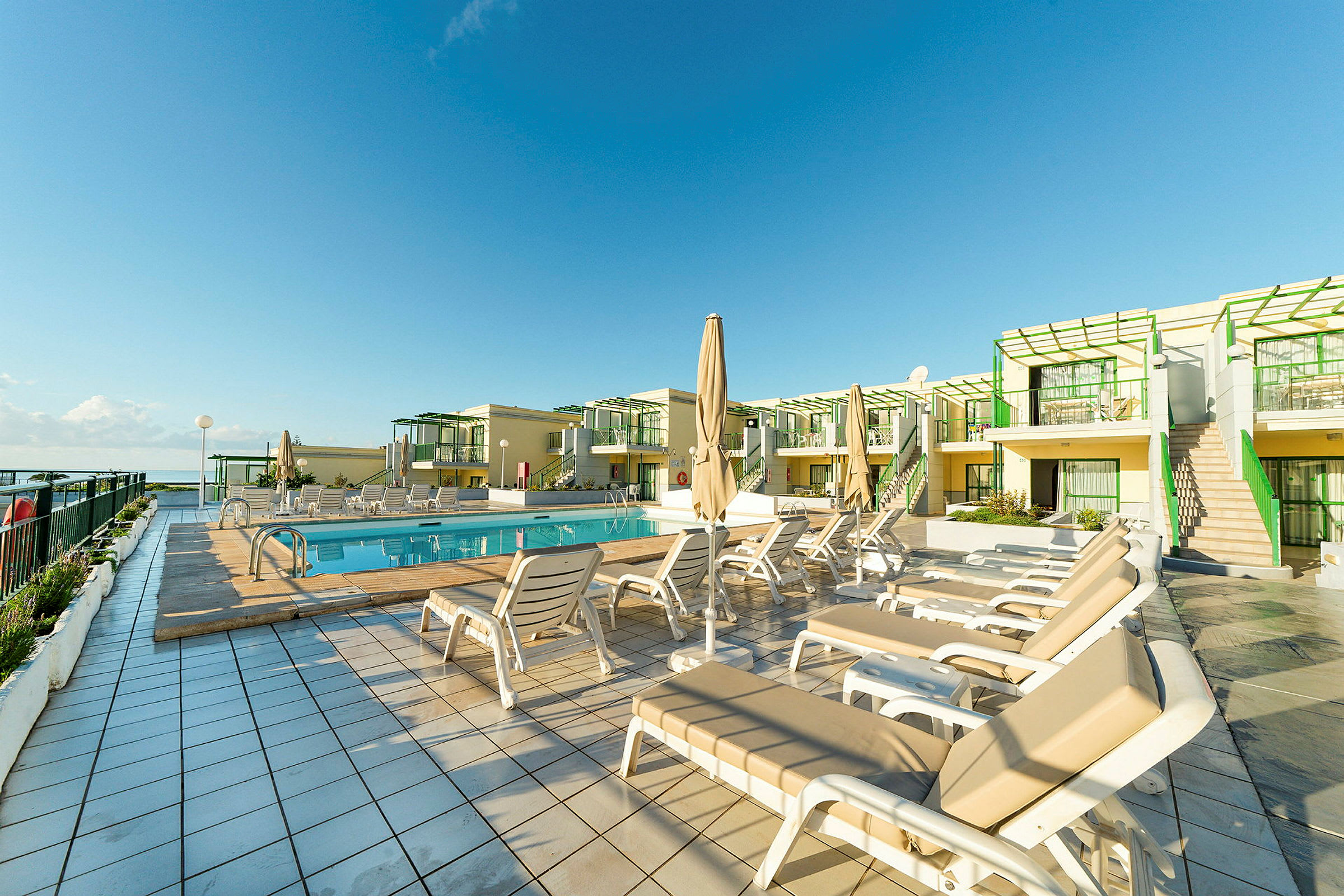 Pool och solstolar framför lägenhetskomplex. (AI-genererad text)