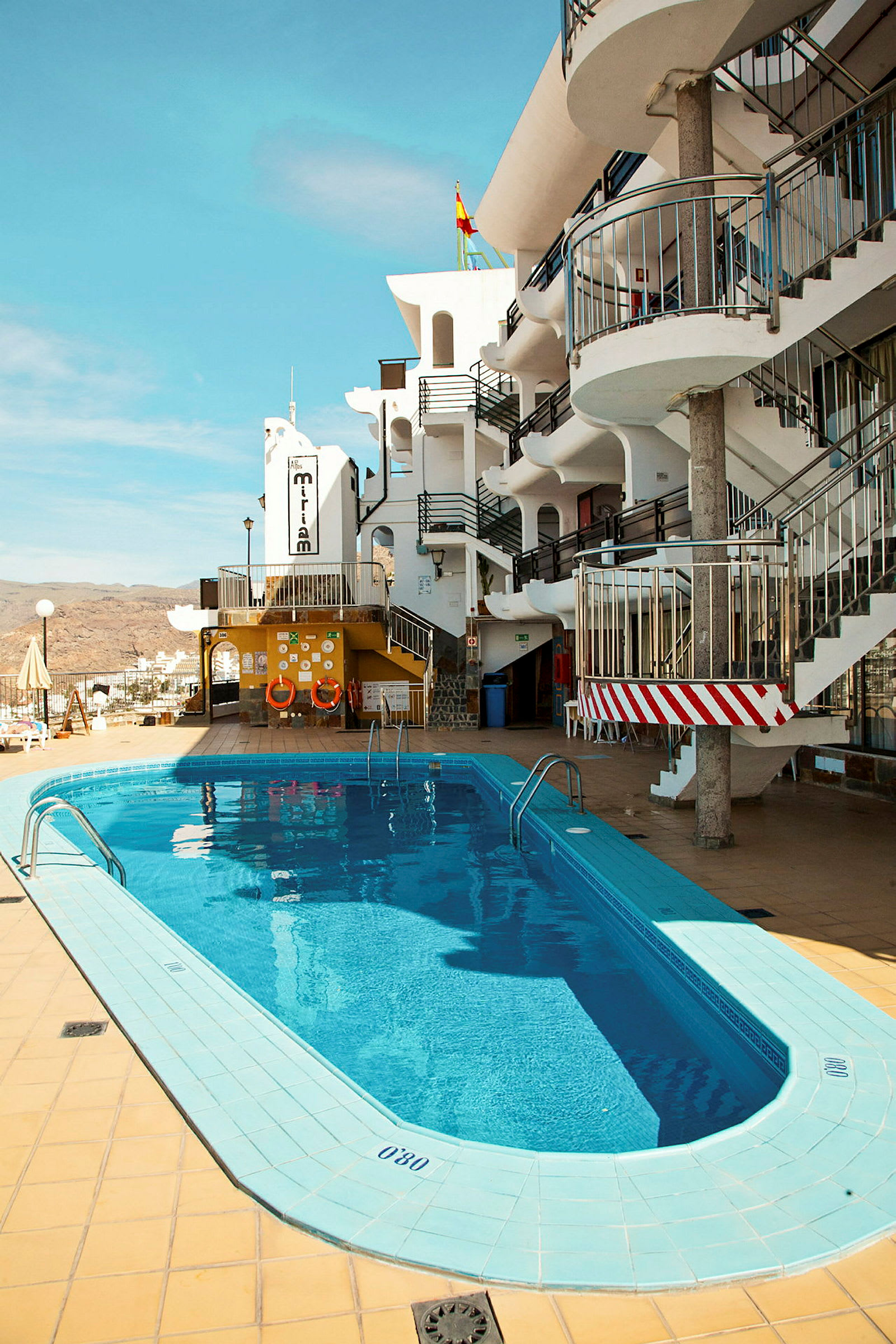 Utomhuspool vid hotell med vit byggnad och blå himmel. (AI-genererad text)