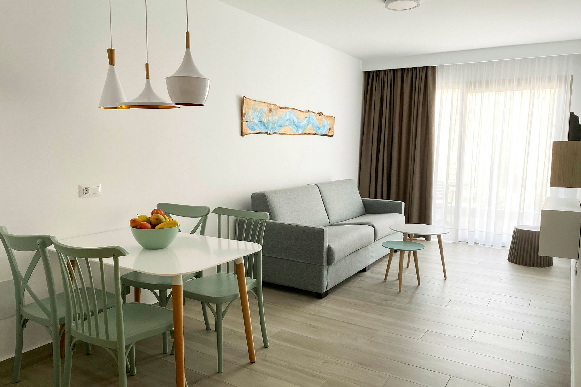 En ljus och modern vardagsrumsinteriör med soffa, matbord och stolar, samt en skål med frukt på bordet. (AI-genererad text)