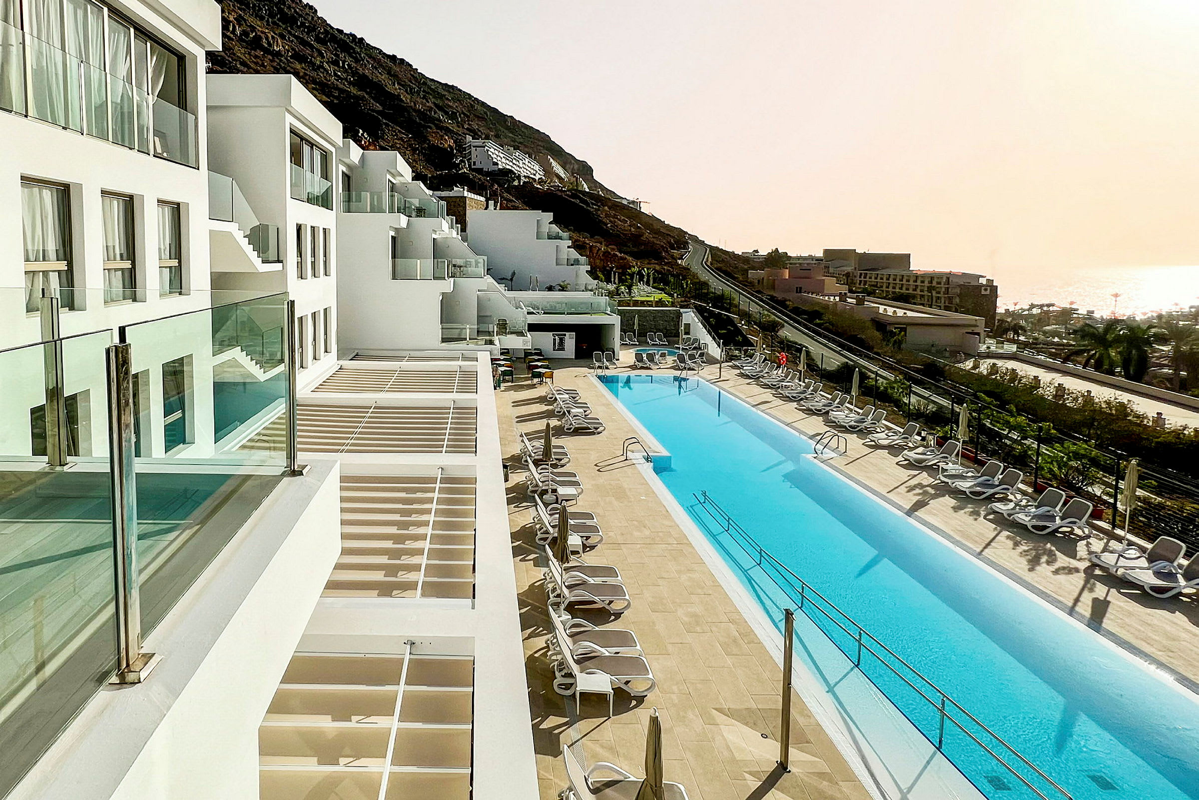 Hotell med vita byggnader och en lång pool omgiven av solstolar. (AI-genererad text)