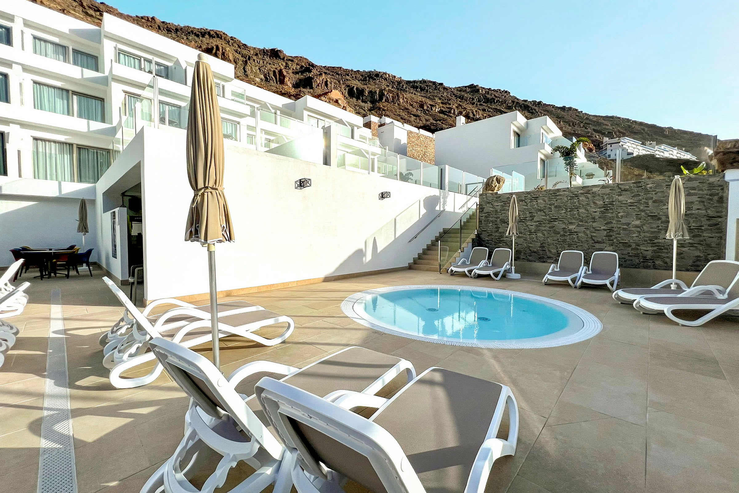 Liten pool med solstolar och parasoller på en terrass vid ett hotell. (AI-genererad text)
