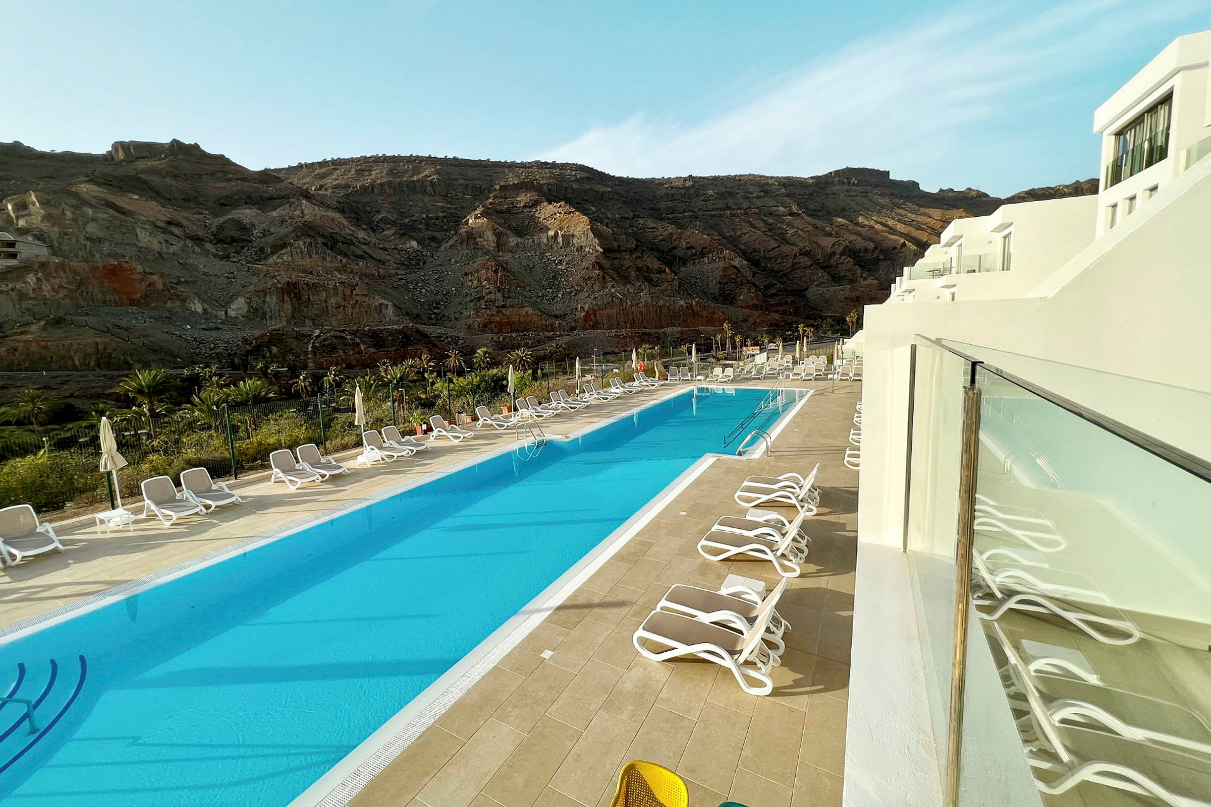 Bild av en pool med solstolar runtom och berg i bakgrunden. (AI-genererad text)