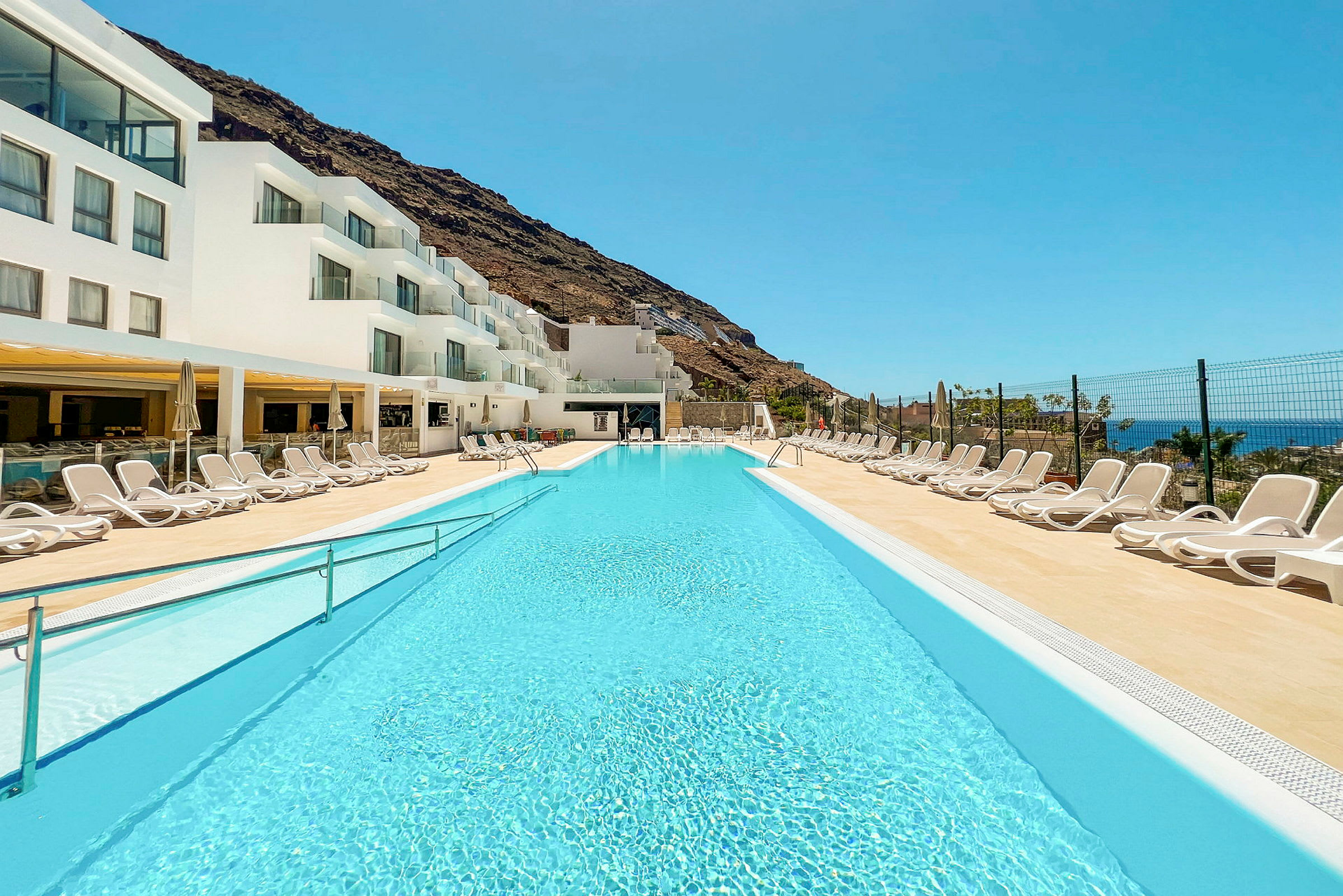 En pool vid ett hotell med vita byggnader och solstolar. (AI-genererad text)