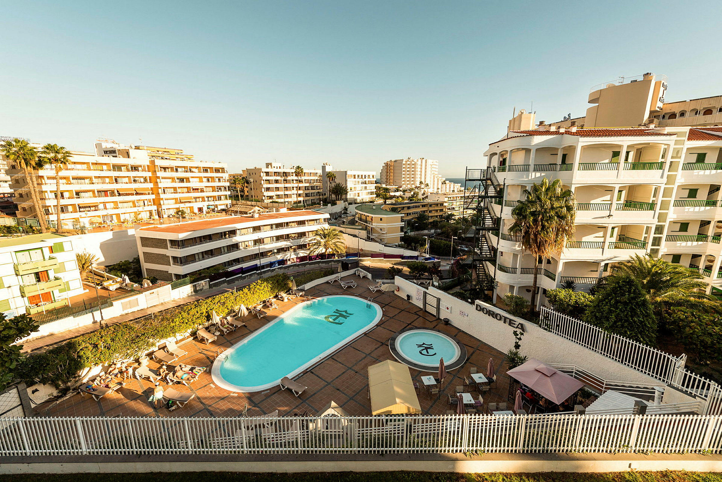 Bild av ett hotellområde med pool och solstolar omgivna av flervåningshus. (AI-genererad text)