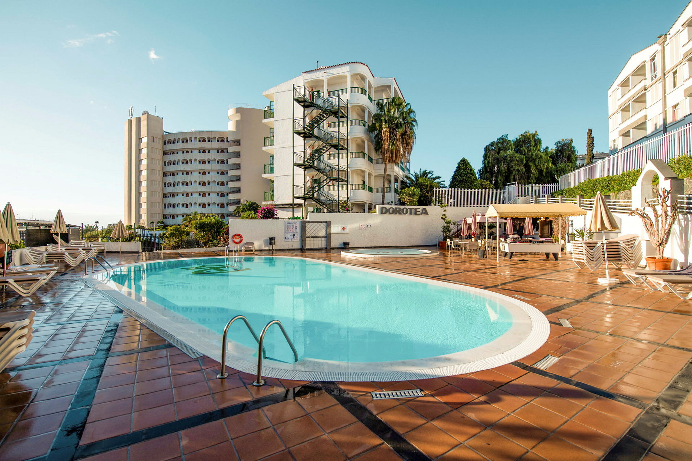 Utomhuspool vid ett hotell med byggnader och solstolar runt omkring. (AI-genererad text)