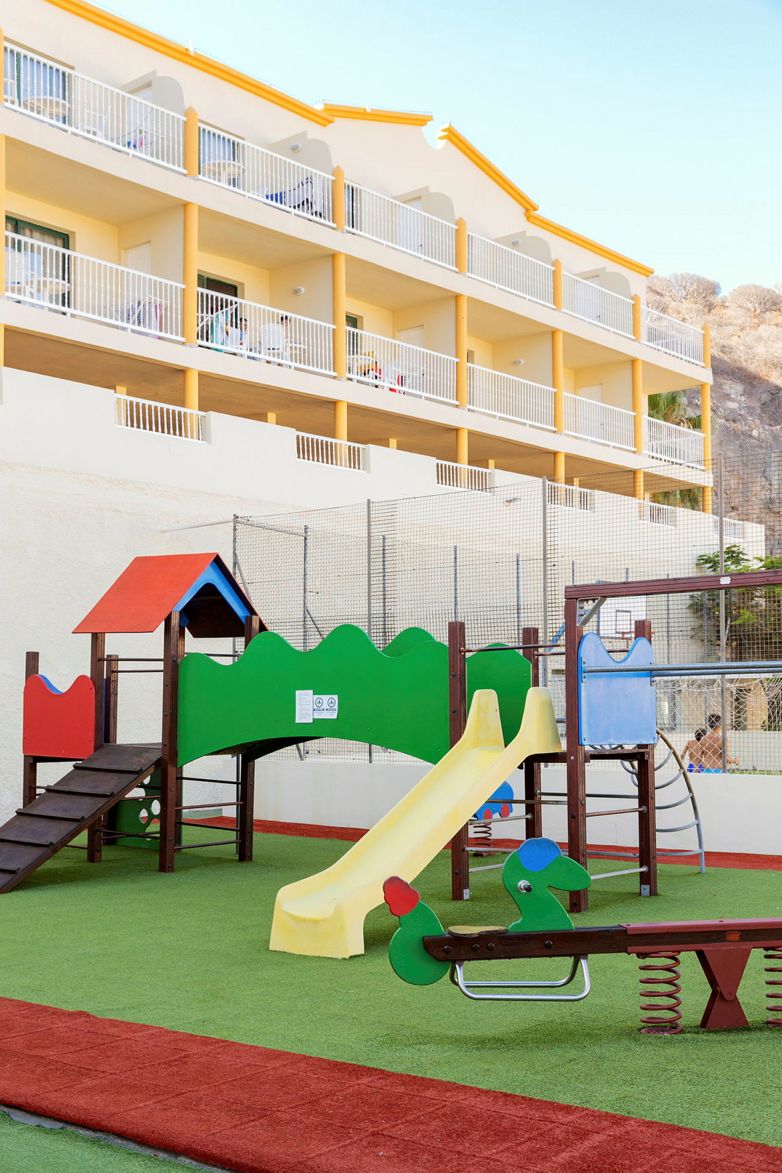 Lekplats med rutschkana och lekutrustning framför en hotellbyggnad. (AI-genererad text)