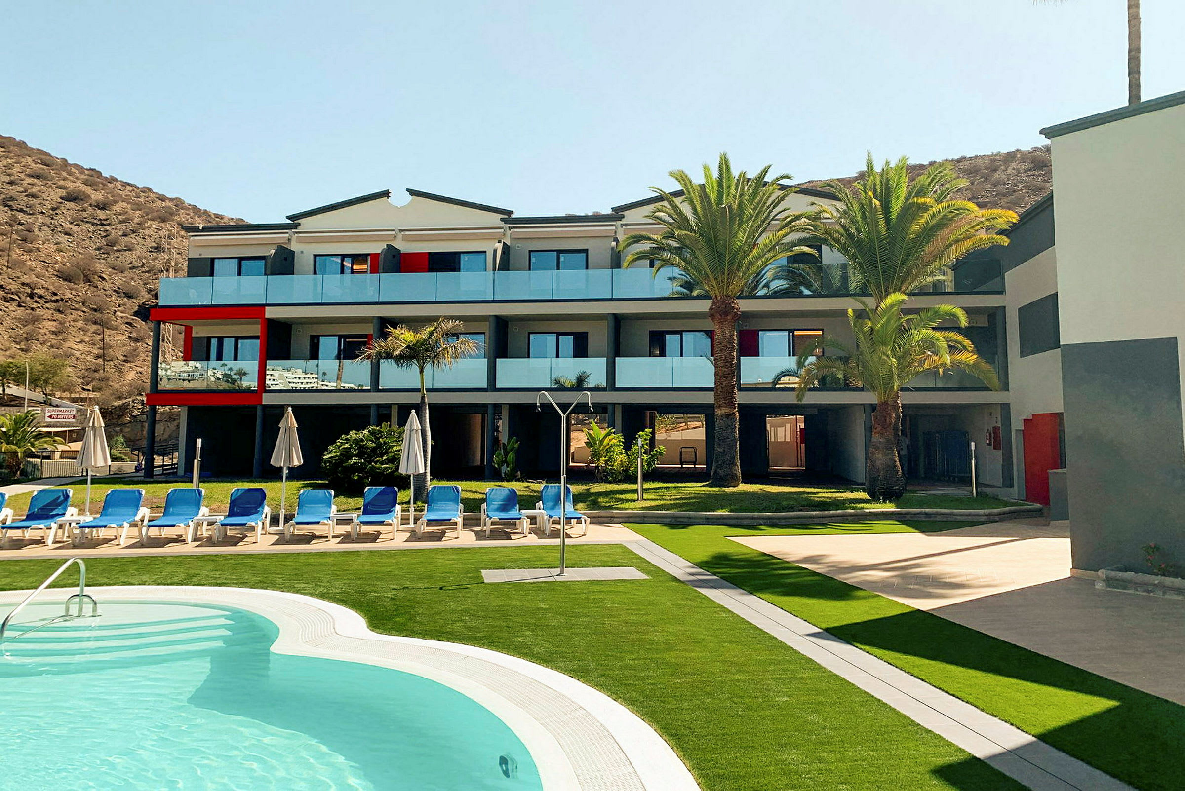 Modernt hotell med pool och solstolar, omgiven av palmer. (AI-genererad text)