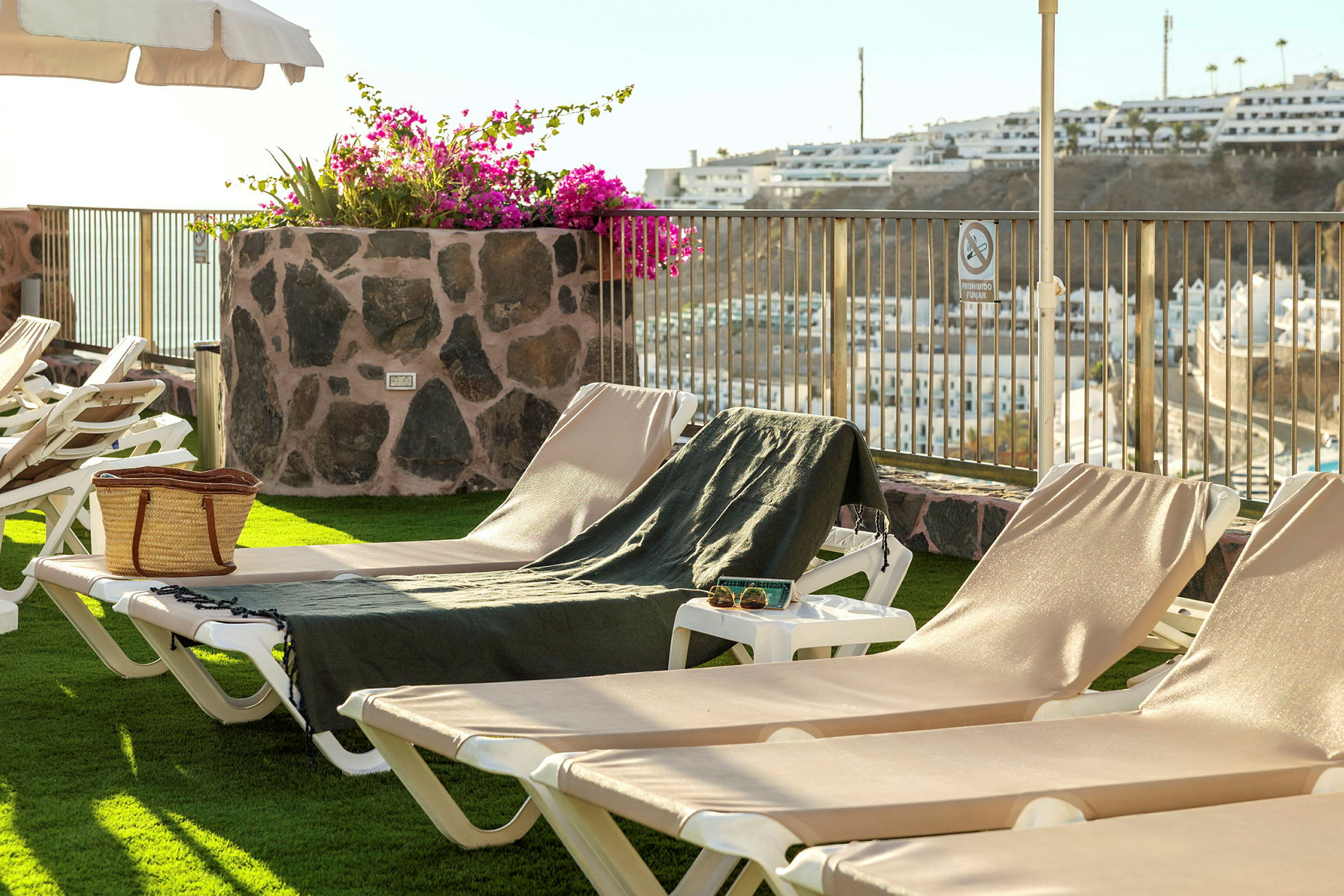 Solstolar på en terrass med utsikt över en stad och blommor i en stenkruka utnyttjas. (AI-genererad text)