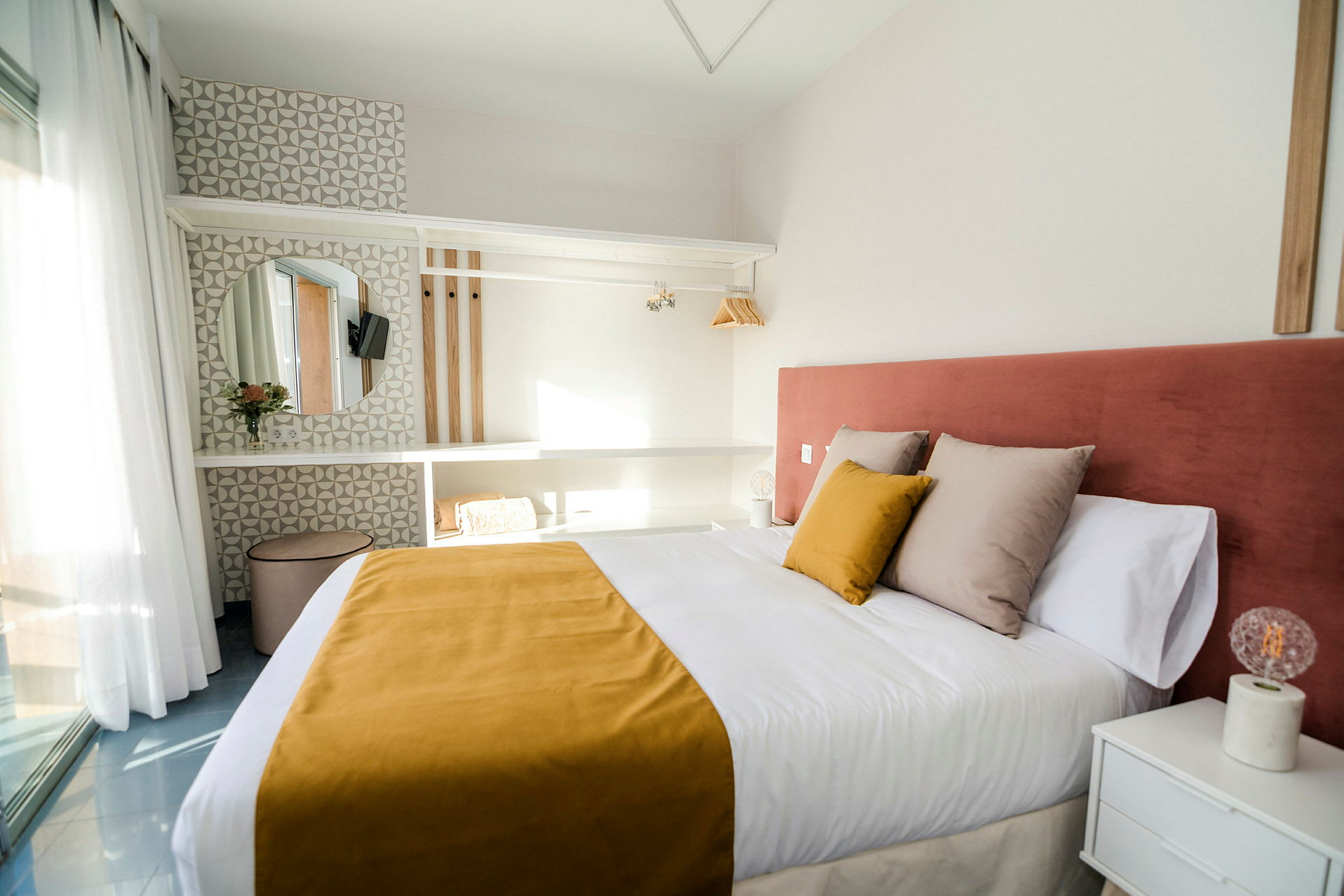 Ett hotellrum med en dubbelsäng, gul sängöverkast och rosa sänggavel, samt en modern inredning med hyllor, spegel och ljus dekoration. (AI-genererad text)