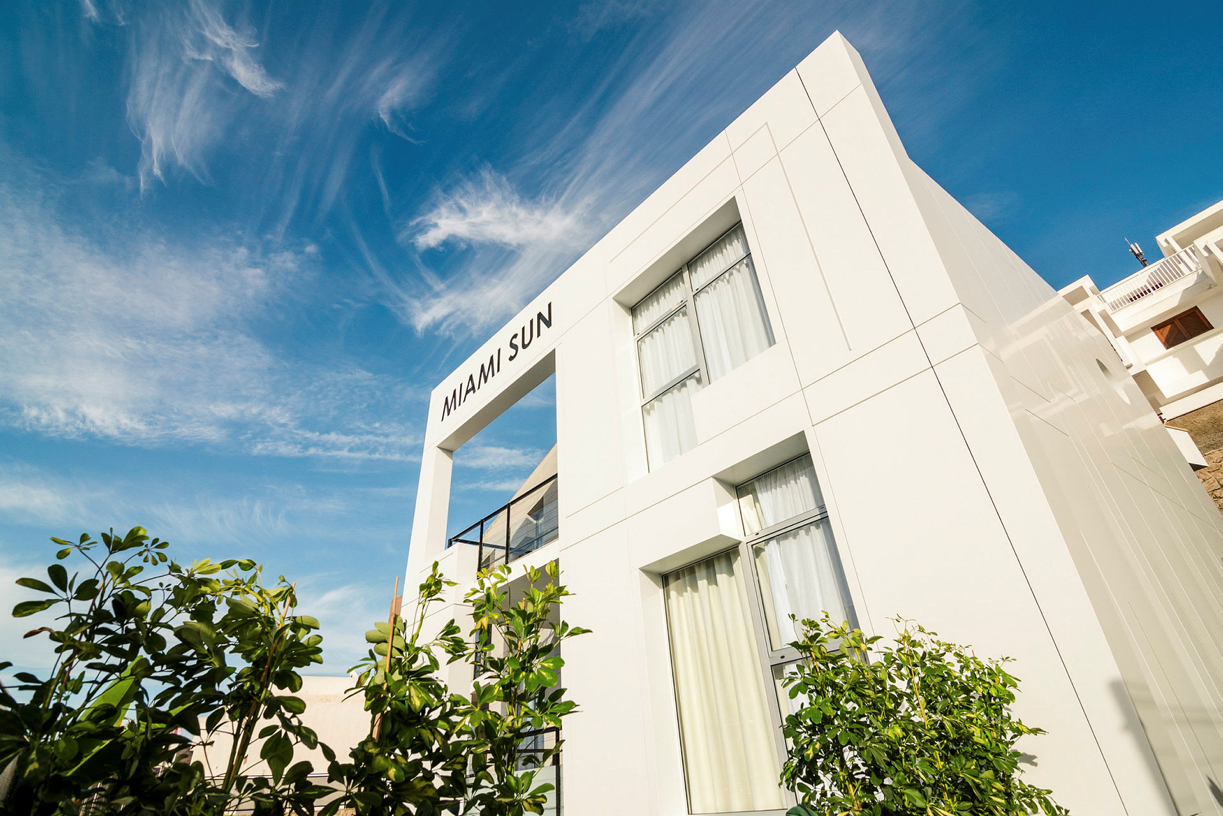 En vit byggnad med texten "MIAMI SUN" på fasaden mot en blå himmel. (AI-genererad text)