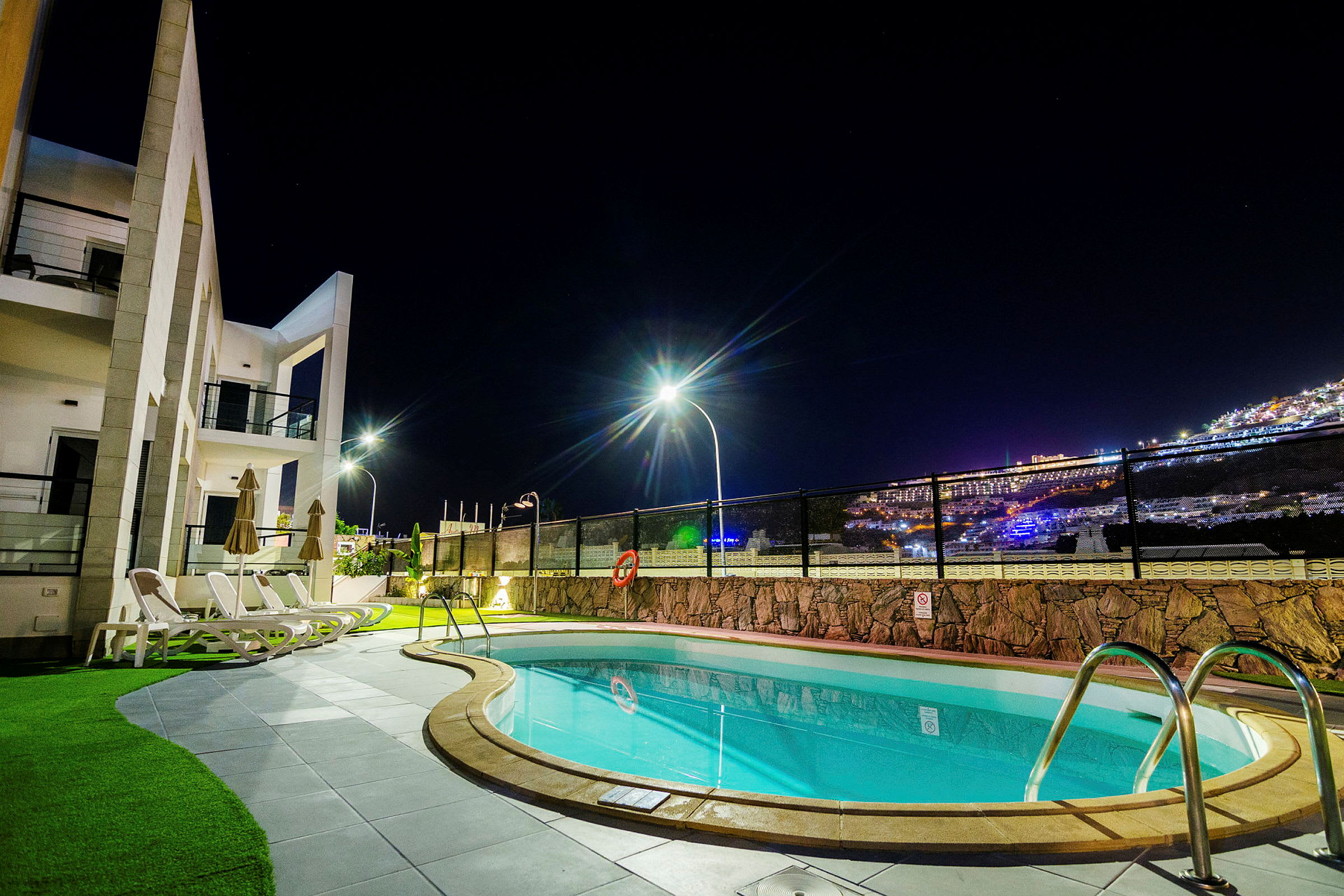 En upplyst pool och byggnad vid natt med stadsljus i bakgrunden. (AI-genererad text)