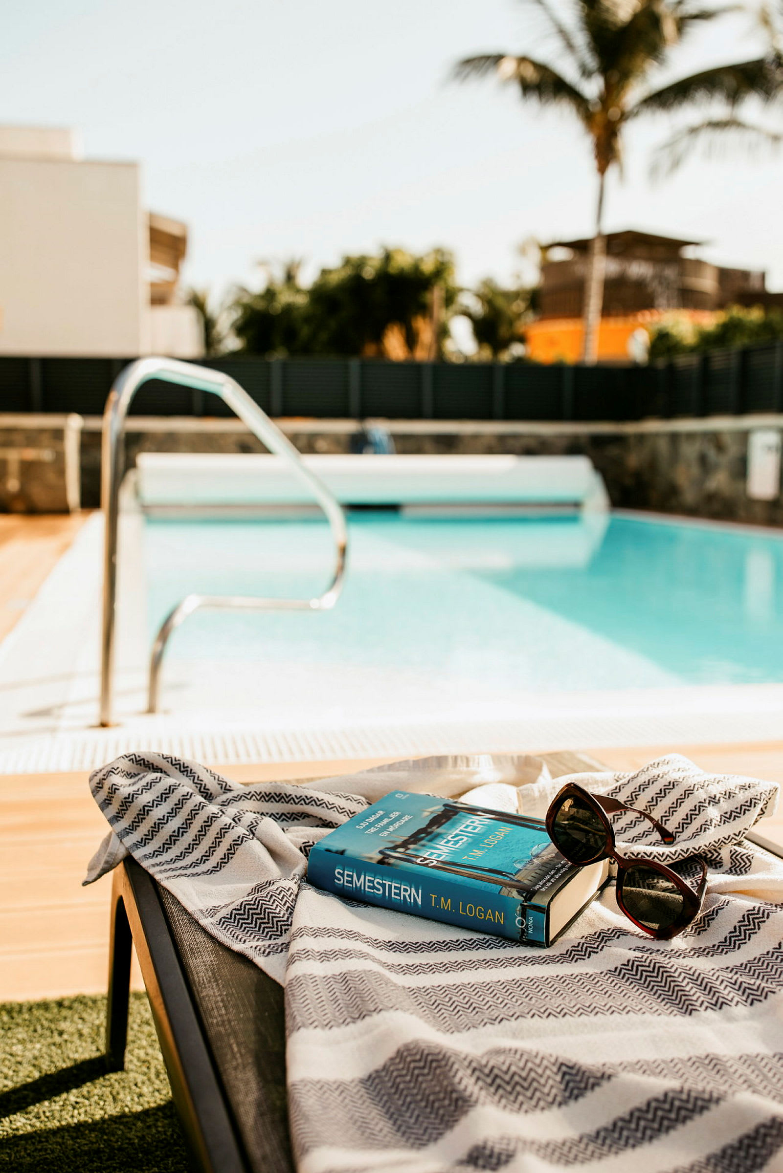 Solglasögon och en bok på en solstol vid en pool. (AI-genererad text)