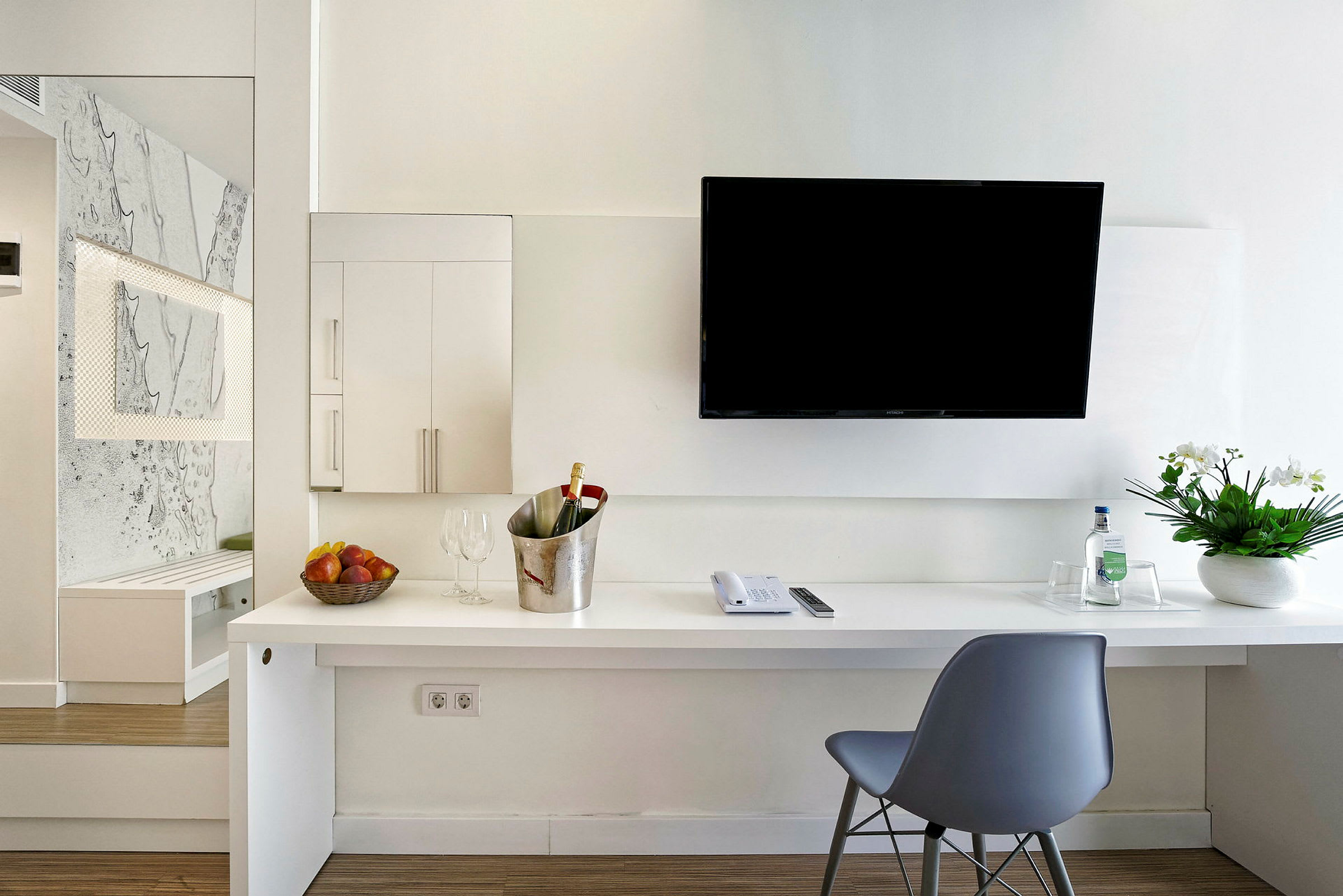 Modern hotellrumsinredning med skrivbord, stol, vägg-tv, blomarrangemang och förfriskningar. (AI-genererad text)
