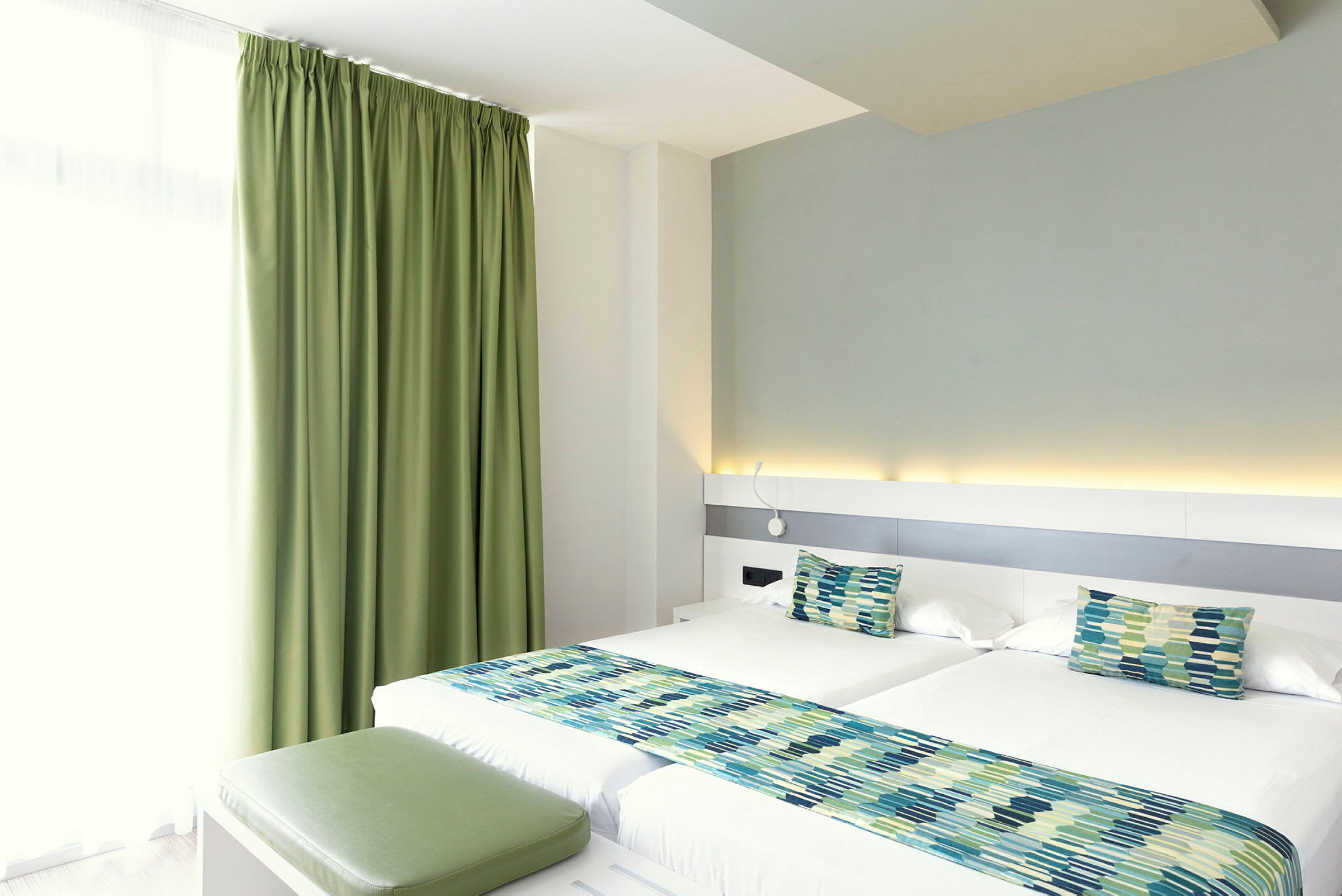 Ett hotellrum med två enkelsängar, gröna gardiner och matchande sängdekorationer. (AI-genererad text)